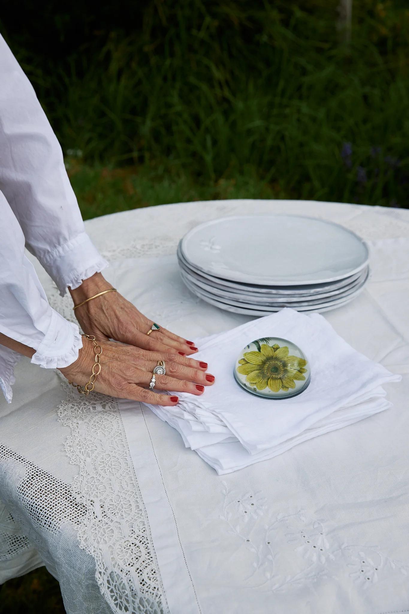 hands place white napkins next to a stack of plates on table set in the garden