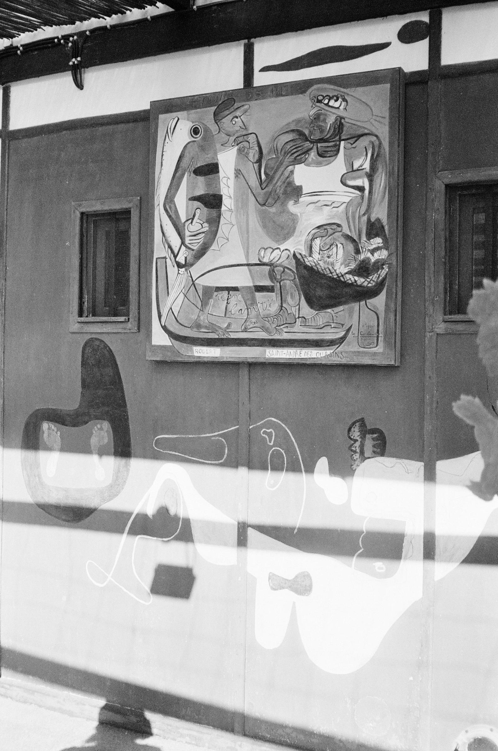 Black-and-white photo of wall with abstract painting. Two small windows and unique painted patterns visible.
