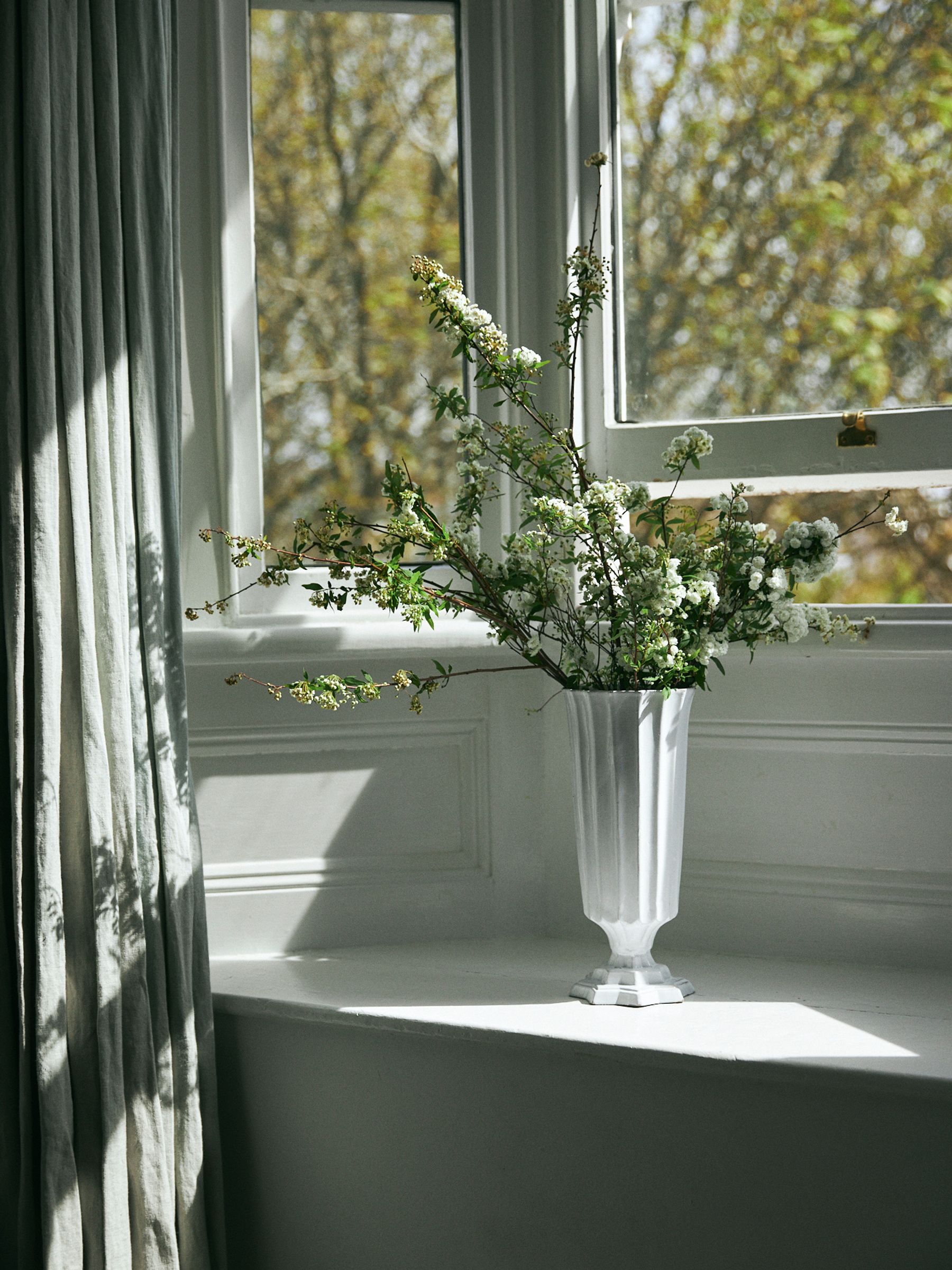 white vase sits on window seat in the sun filled with flowers