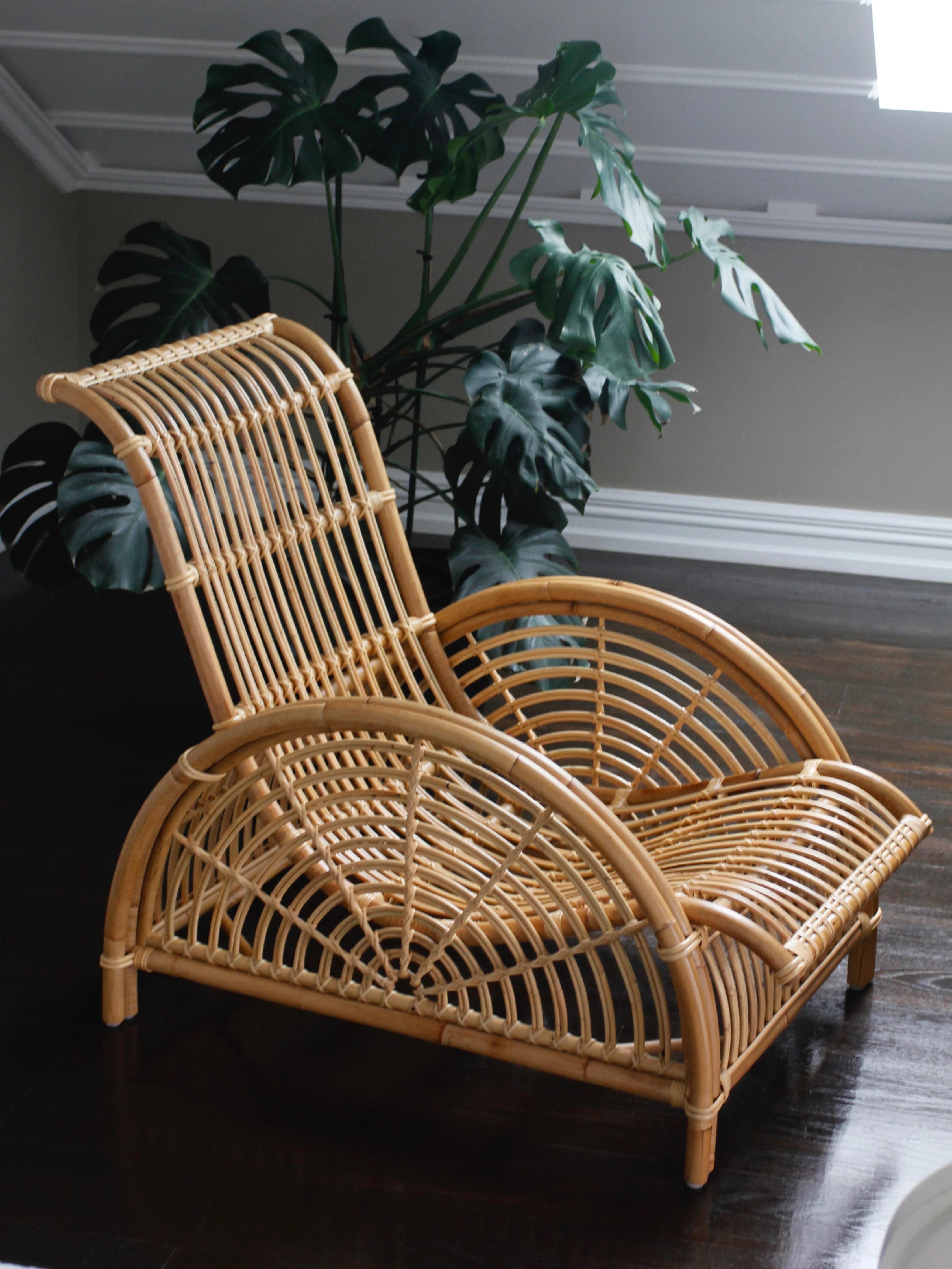 A modern rattan chaise lounge with a curved design on a dark wooden floor, set against large monstera leaves that add a natural touch.