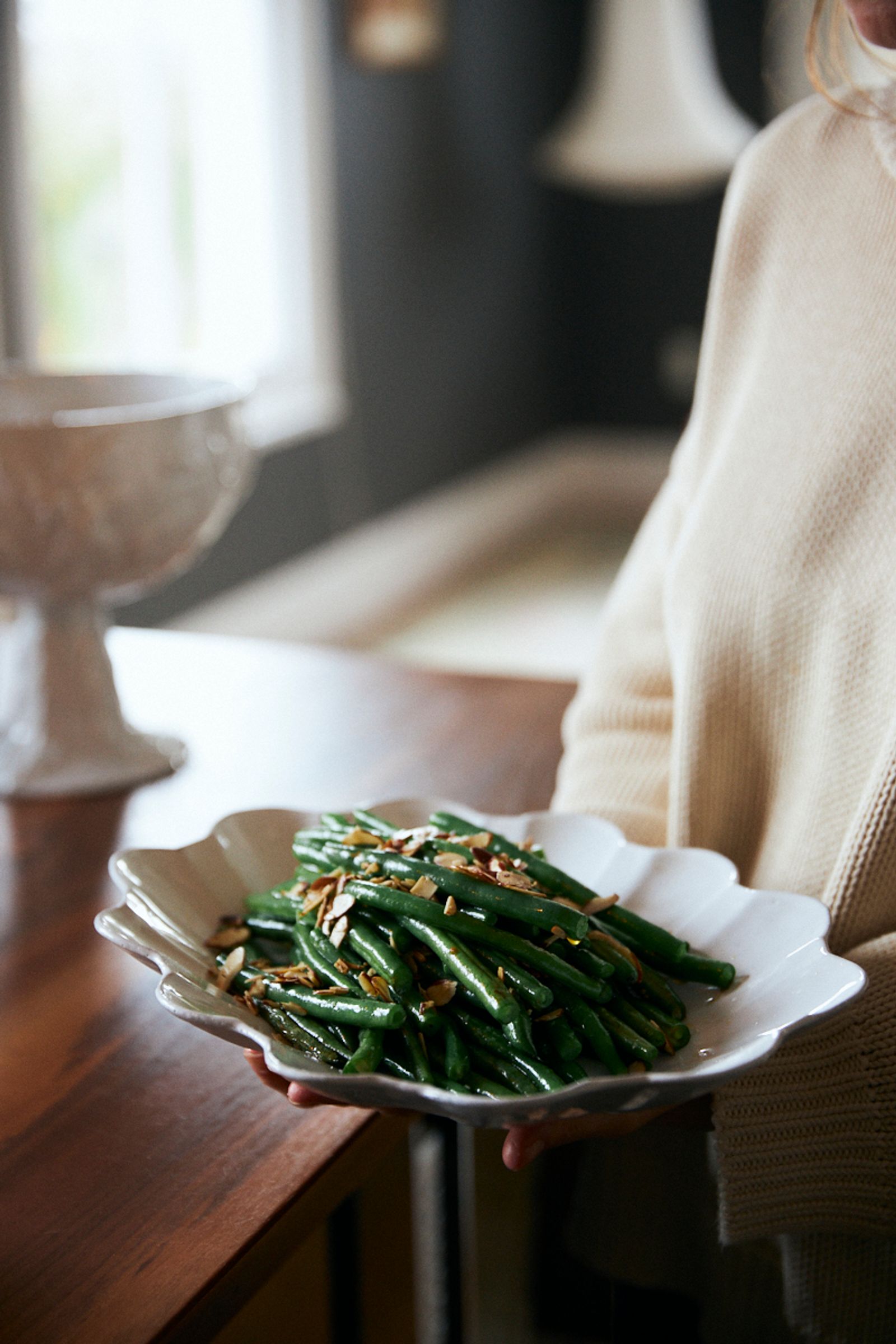 woman holds a ceramic platter with steamed green beans in a kitchen setting