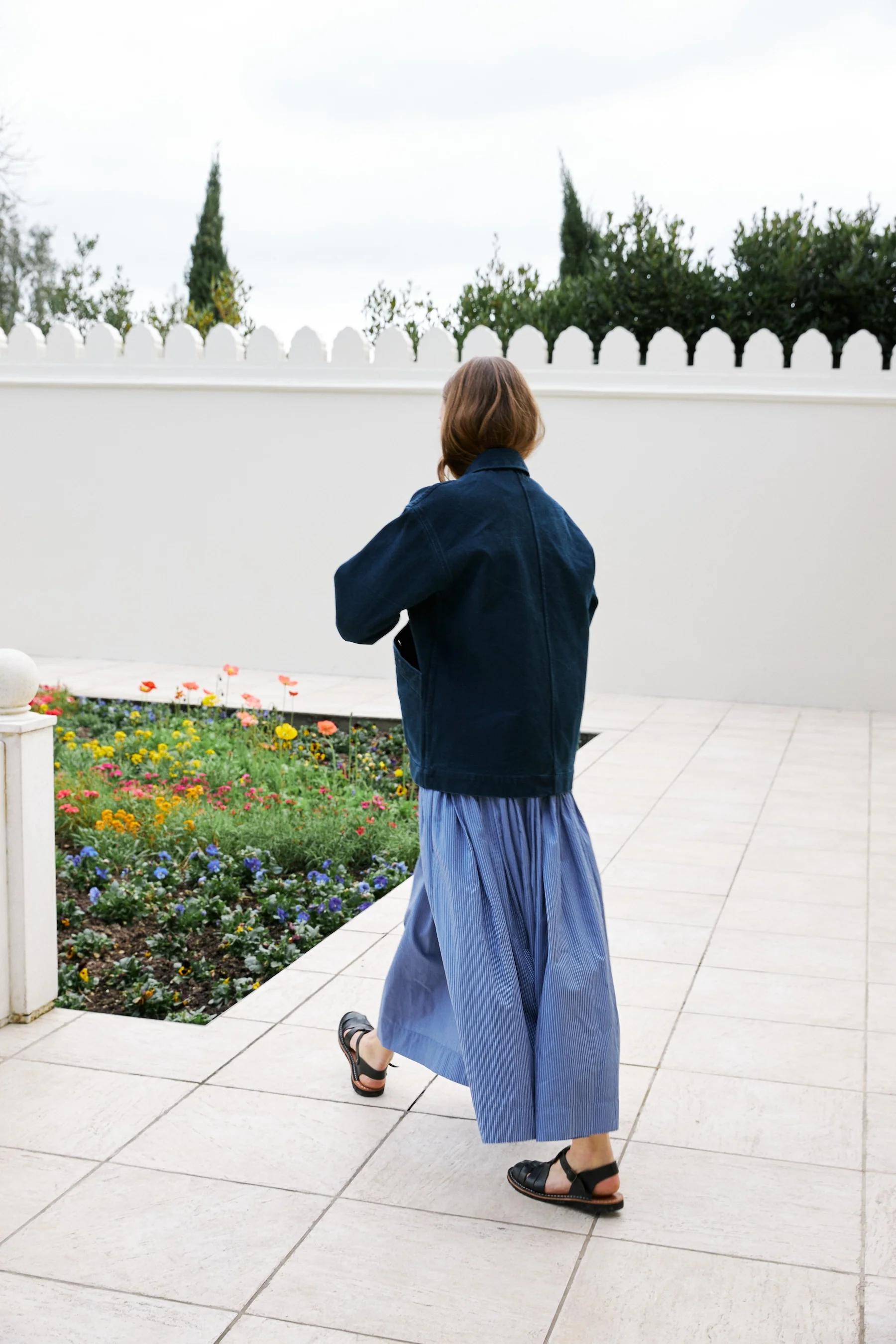 Oversized indigo jacket is worn over a blue skirt with black sandals.