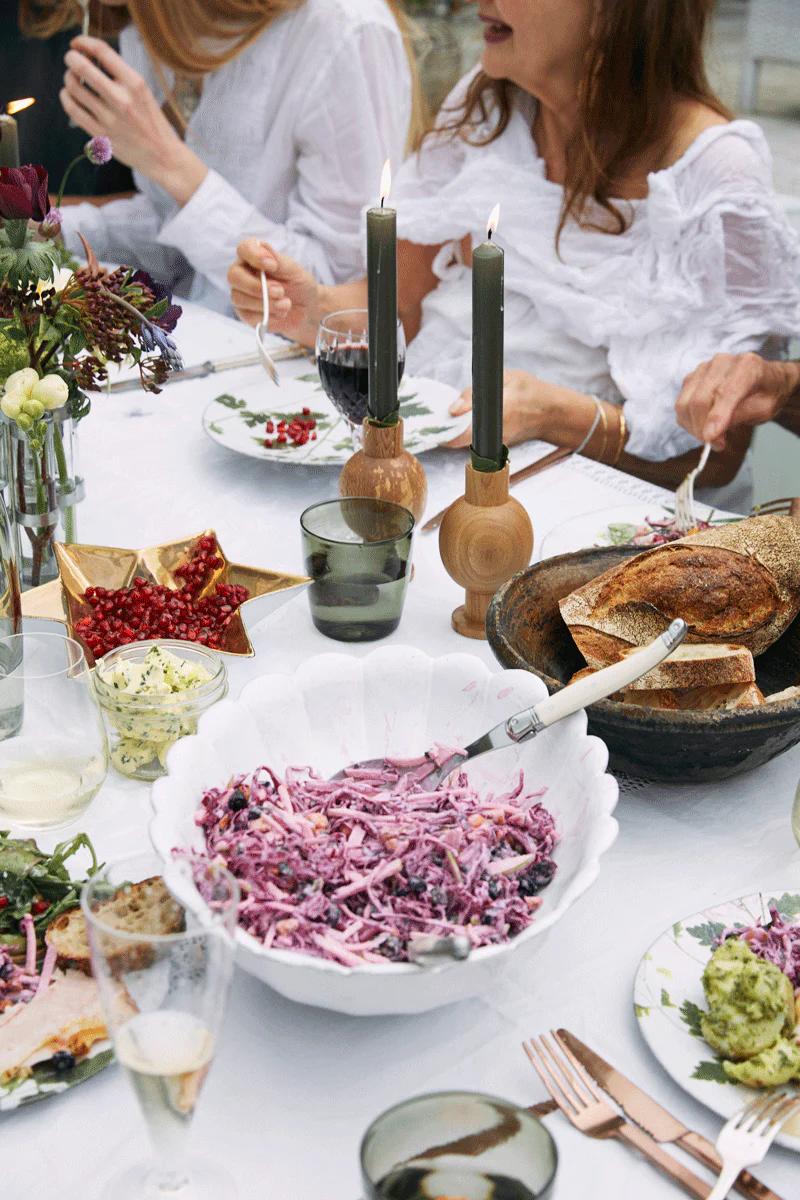 Outdoor table with purple coleslaw, bread, and salads. Two lit candles in wooden holders.