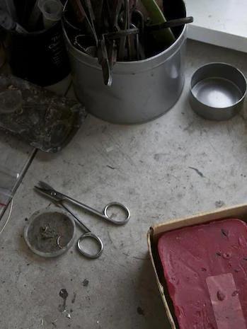 Cluttered workspace: scissors, dish with nails, tool container, red block. Surface covered in dirt and debris, mirroring nature's chaos.