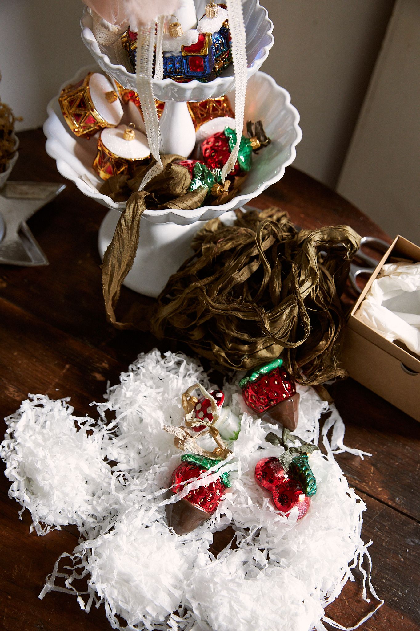 A wooden table hosts piles of silk ribbon and shiny ornaments