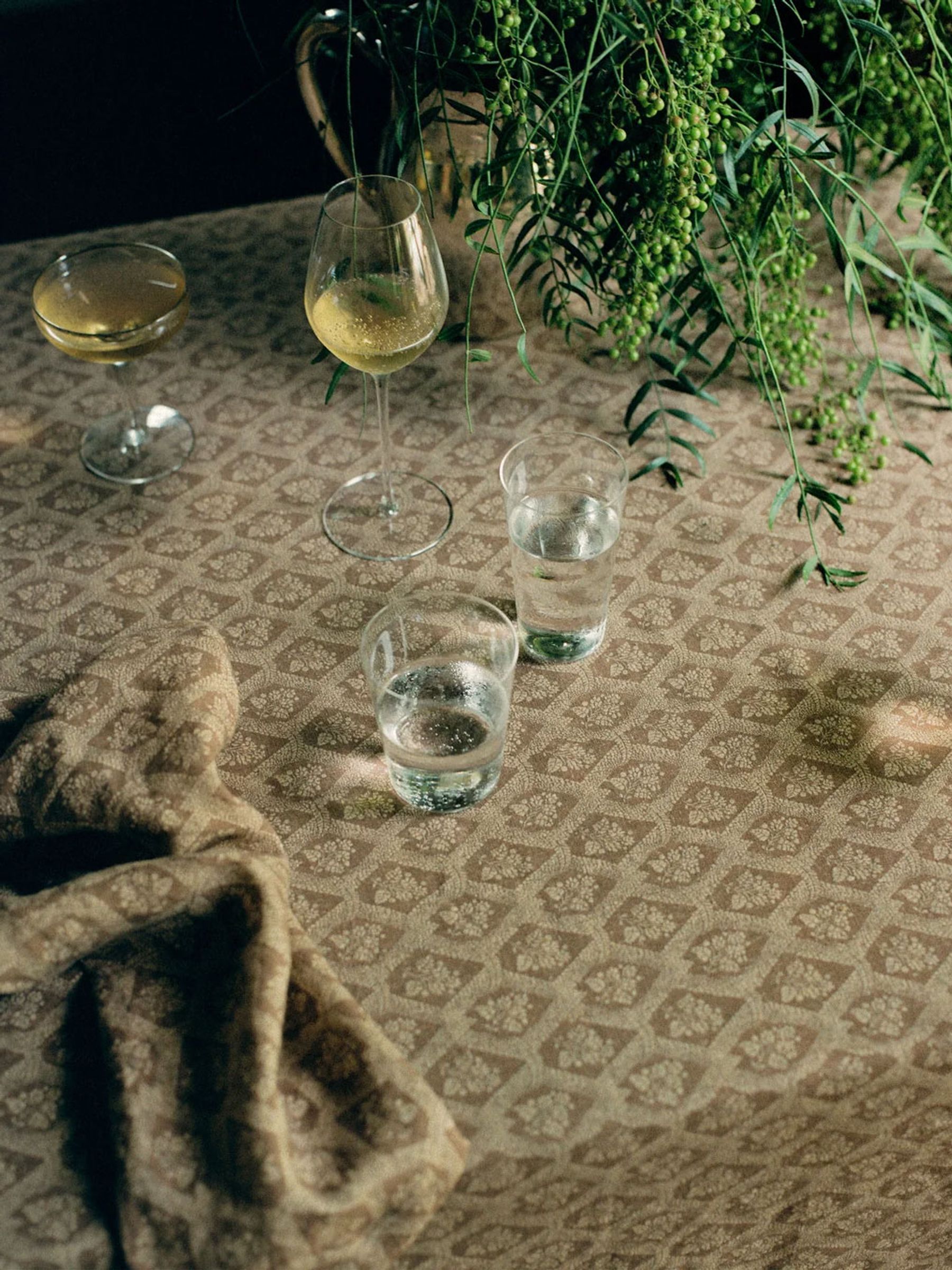 printed table cloth with wine glasses and water glasses next to a vase filled with greenery