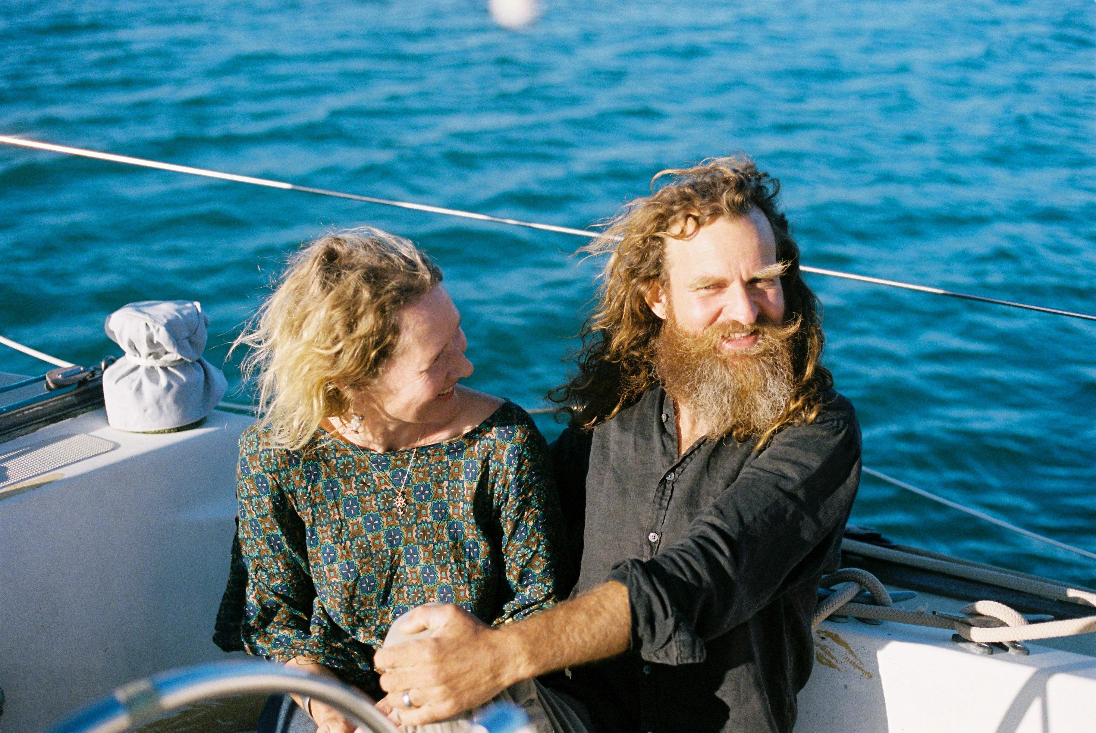 Man with beard and woman sitting on boat near Waiheke Island. Both smiling on sunny day.