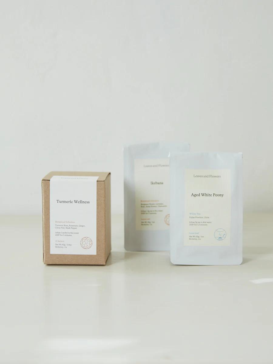 Three tea packages: "Turmeric Wellness" box, "Isabella" and "Aged White Peony" packets. Premium small batch teas from Leaves and Flowers.