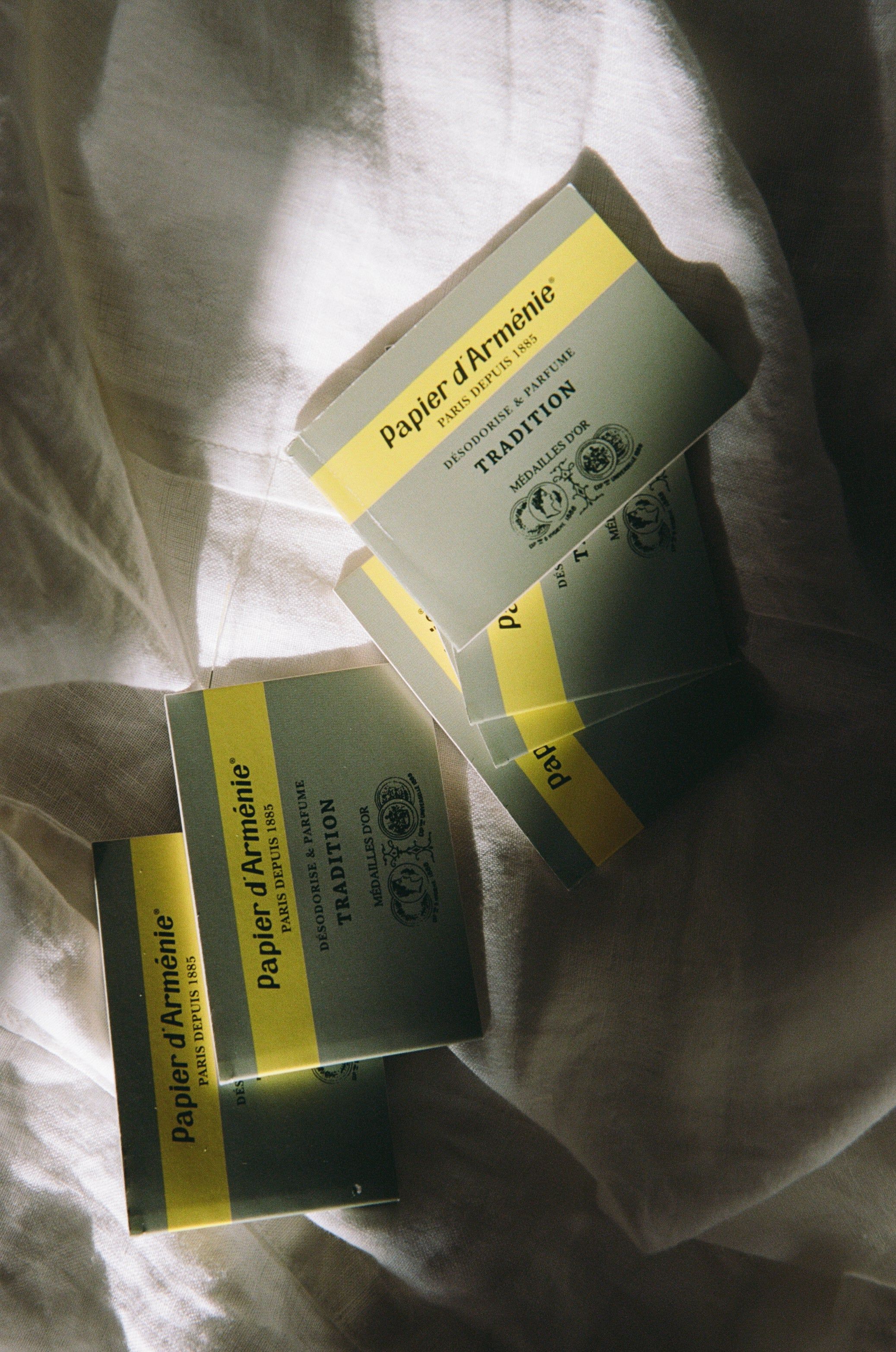 Soft-focus photo of green and yellow Papier d’Arménie booklets scattered on fabric. Gentle light highlights the text and design, creating a peaceful, aesthetic composition.