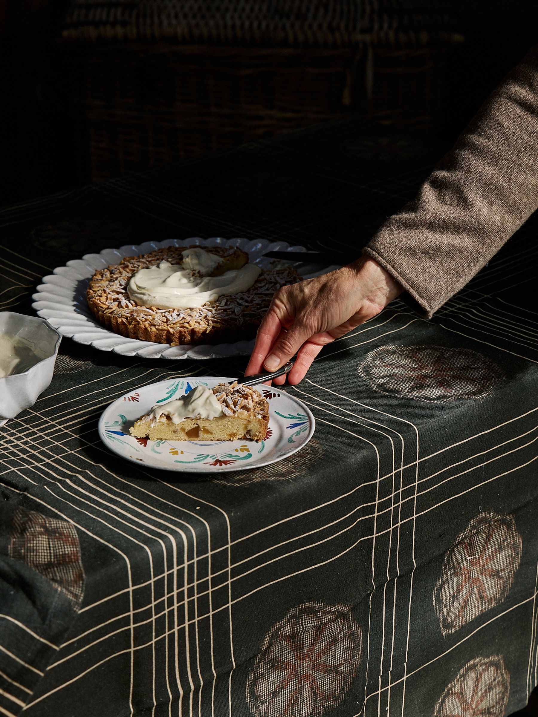 dark tablecloth in natural light with hand serving cake on a plate