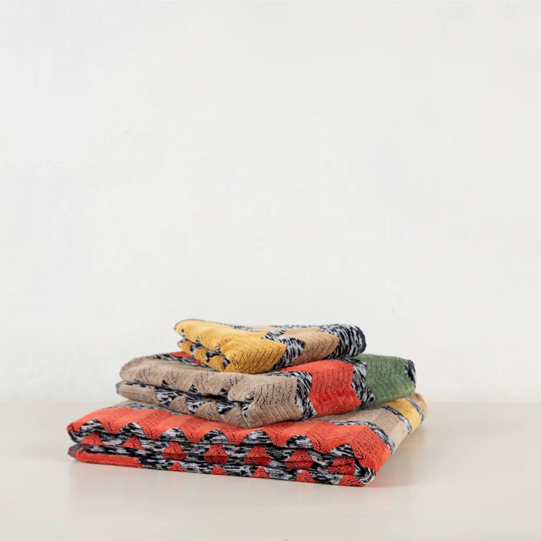 Three folded Missoni blankets with varied patterns. Explosion of colours including orange, yellow, green, beige, and black on light surface.