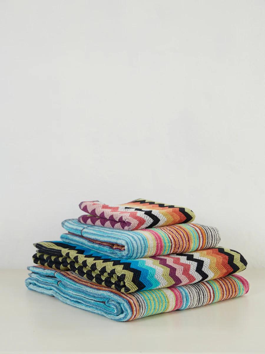 Colourful folded towels with vibrant zigzag patterns in blue, pink, orange, green, black, and white. The luxurious Missoni set rests on a white surface.