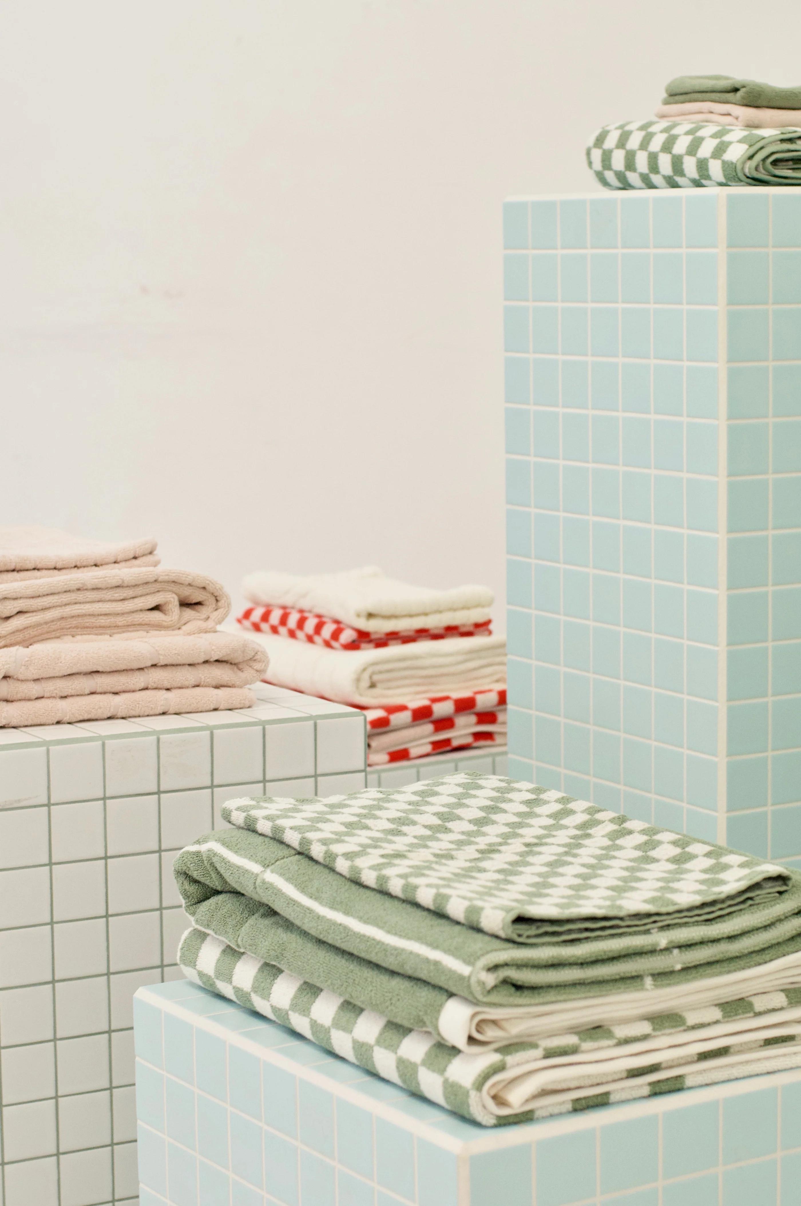 Folded towels on light blue pedestals. Green and white checks, solid pastels, red and white checks. Light-colored wall background.