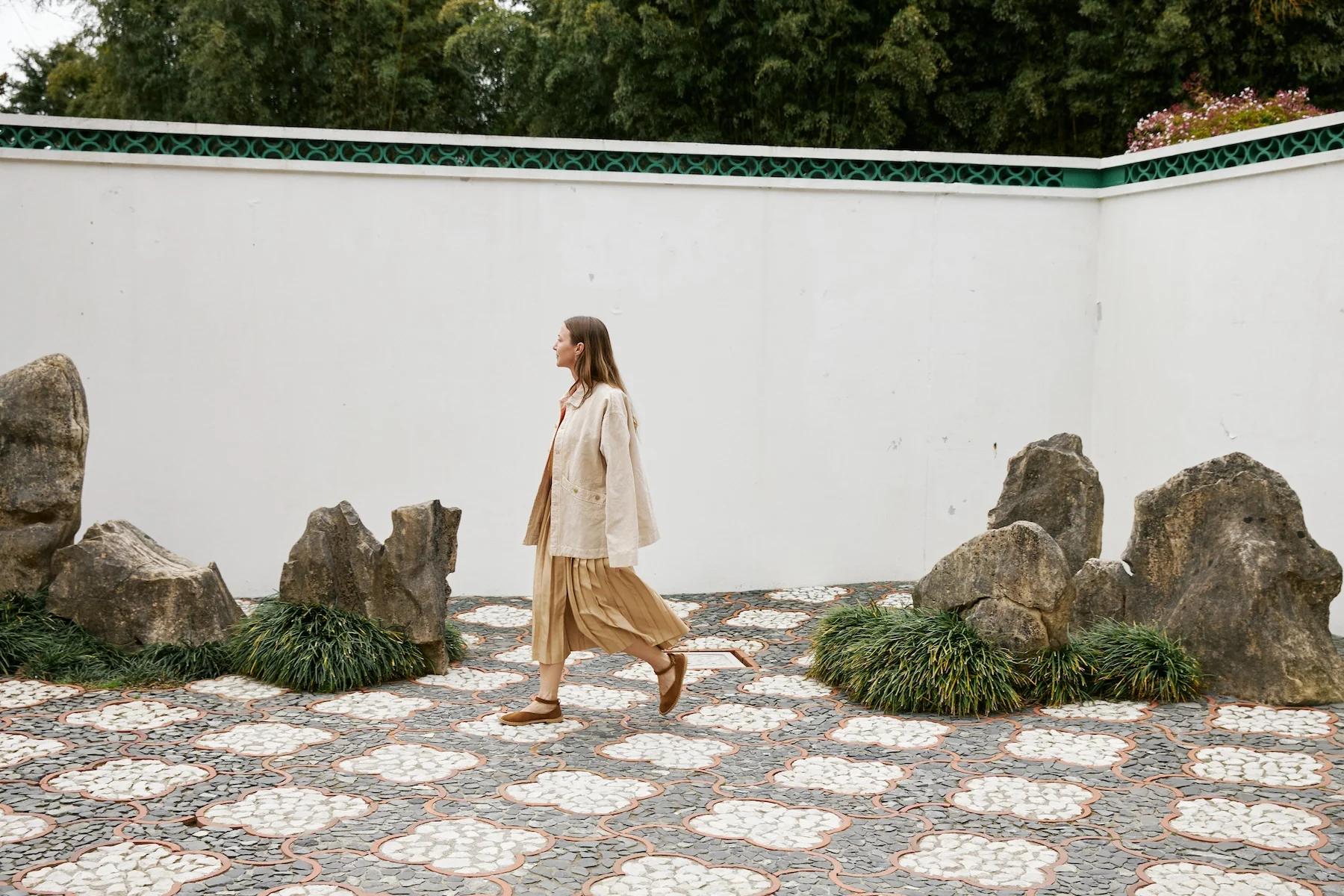 Cream jacket worn loose and open over a pleated skirt walking through the rock garden.