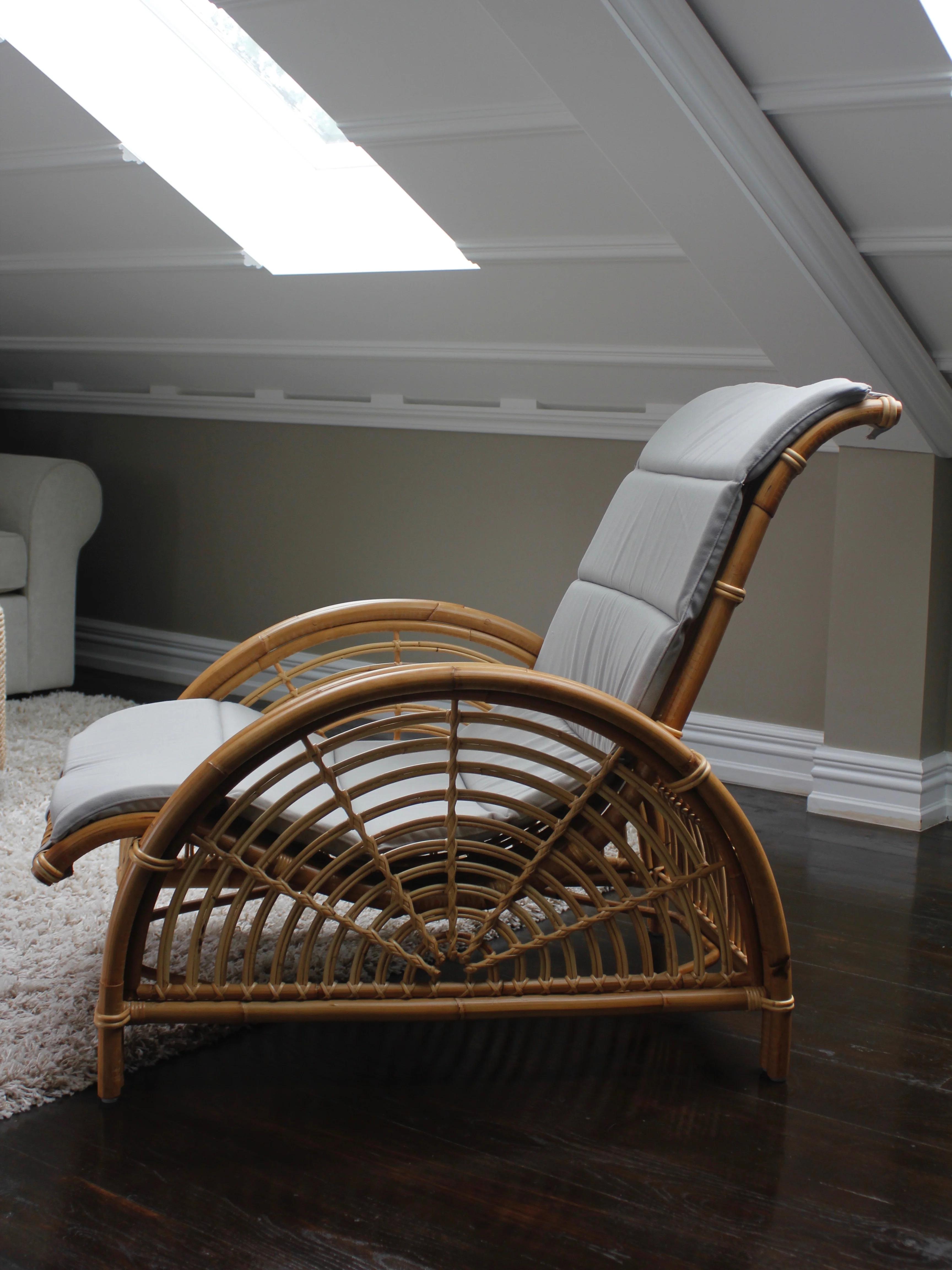 A bamboo lounge chair with a soft cushion on a dark hardwood floor in an attic room, set next to white rattan furniture and a skylight.