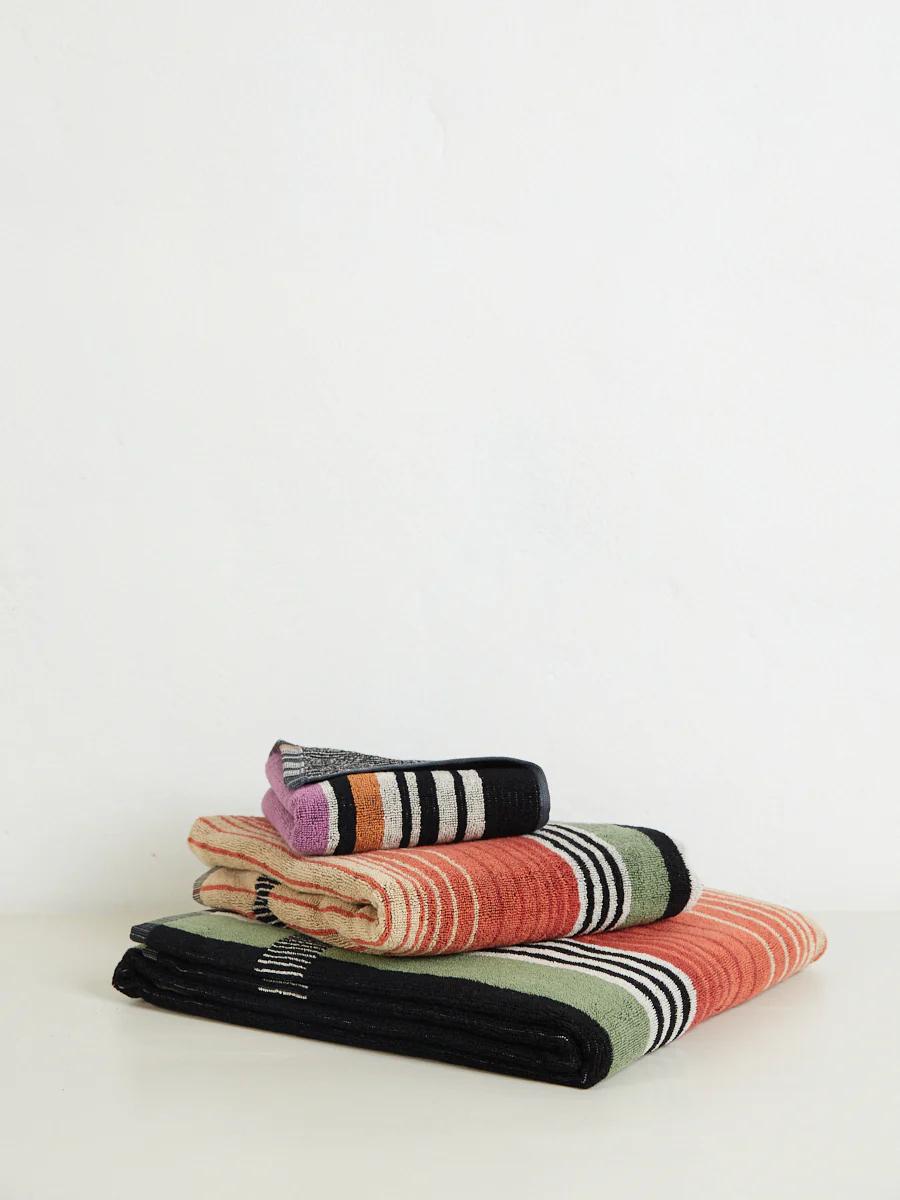 Stacked towels in various colours and sizes with horizontal stripes in orange, black, green, gray, and purple, on a white surface.