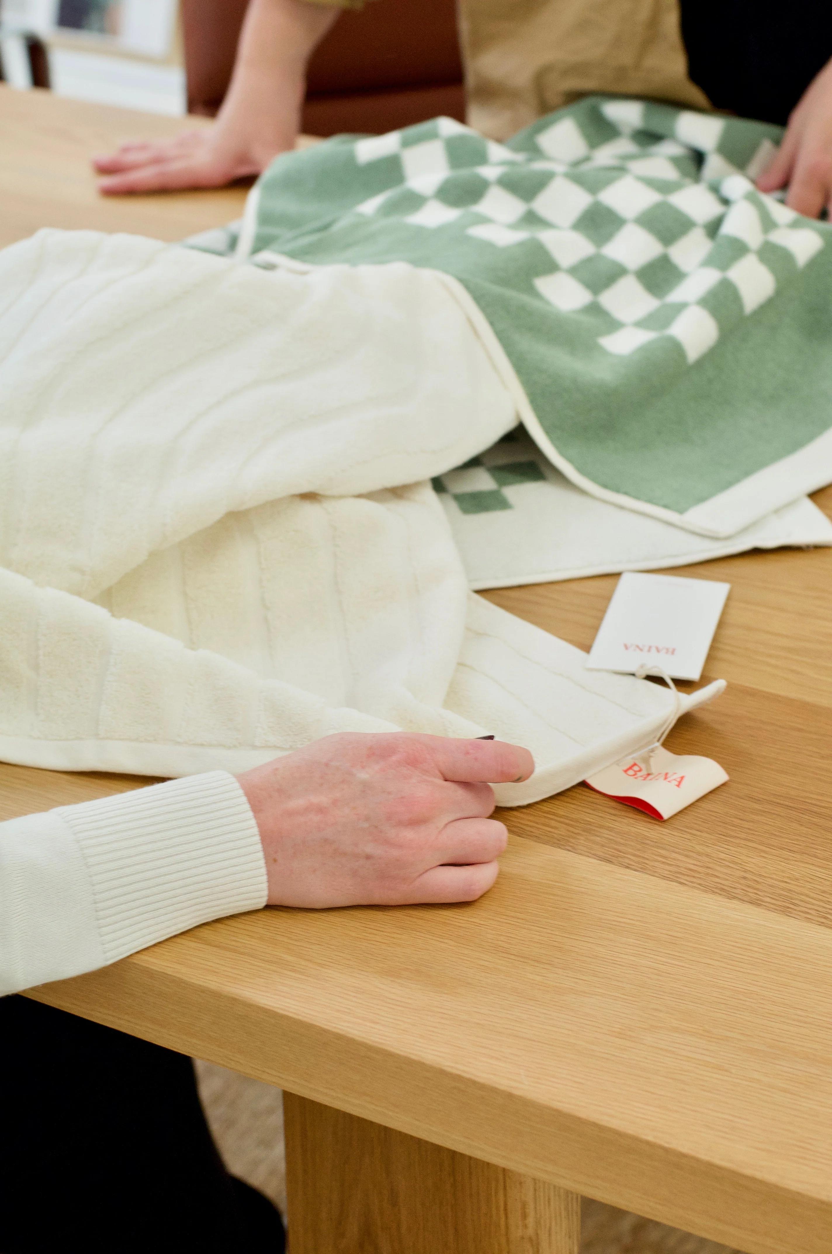 Person holding white towel, examining price tags. Green checkered towel nearby. Another pair of hands in background.