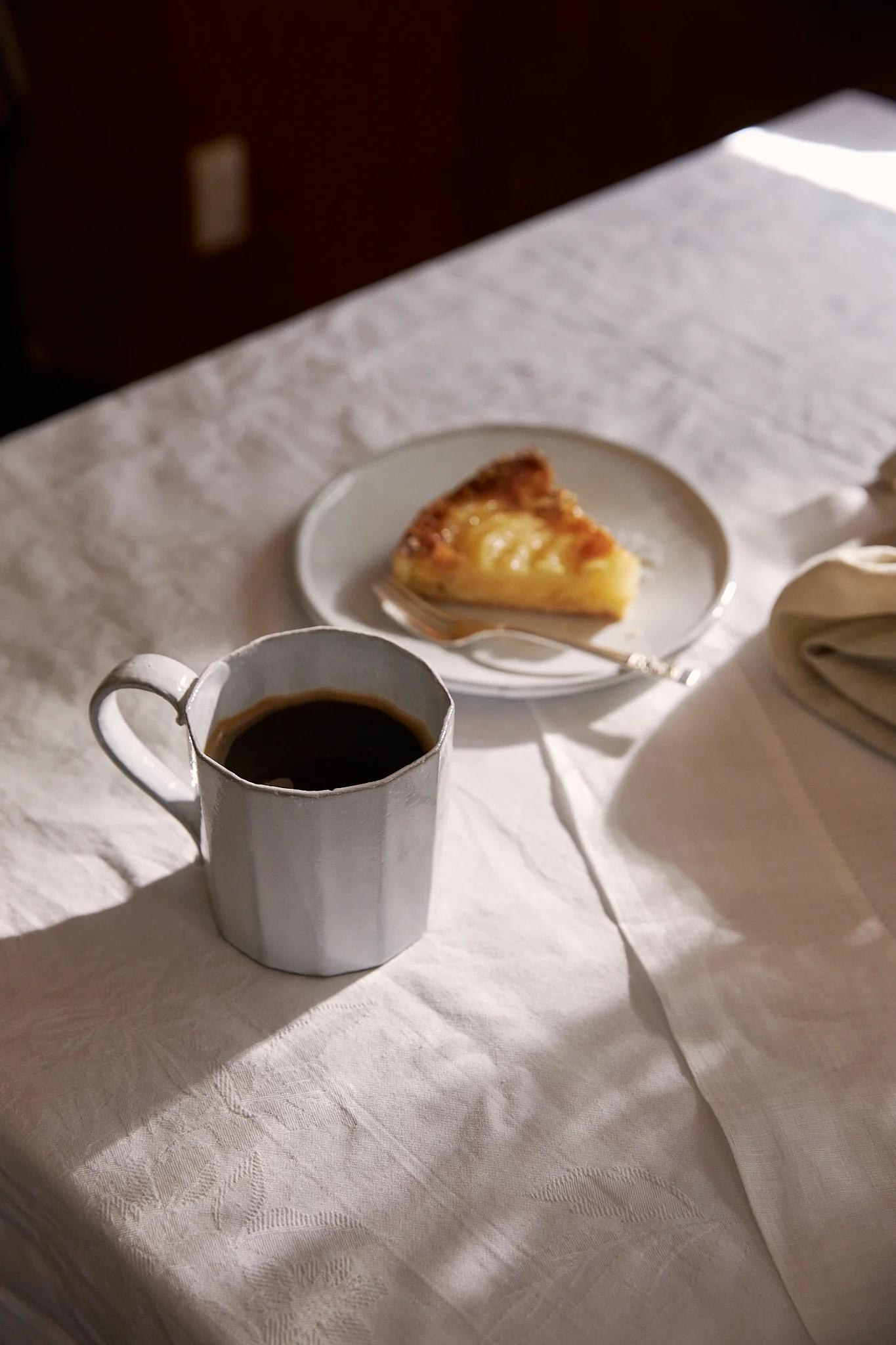 A cup of black coffee sit in a slant of dappled sunlight 