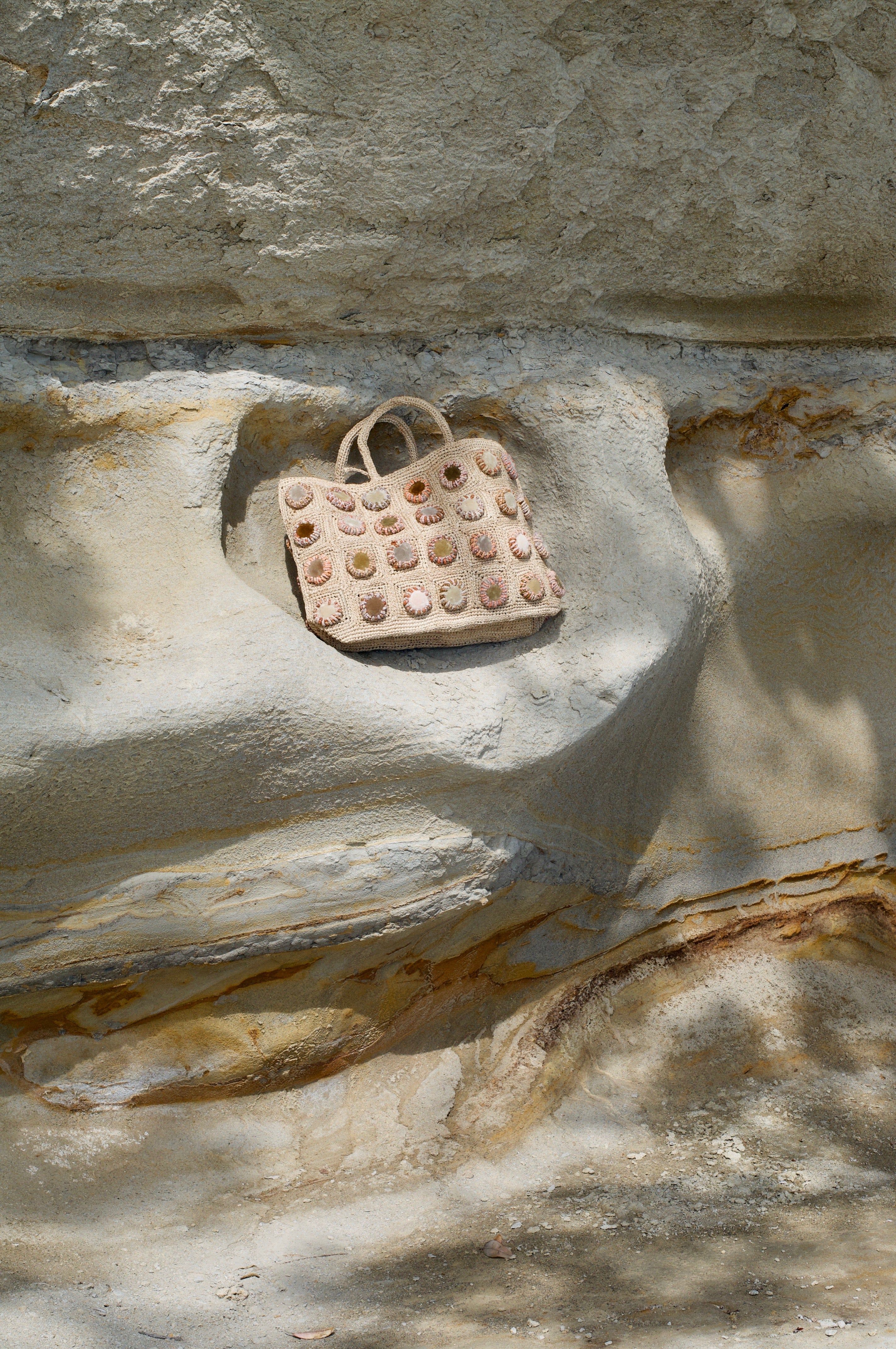 Light-coloured handbag on rocky beige surface. Eroded rock background with shadows and patterns.