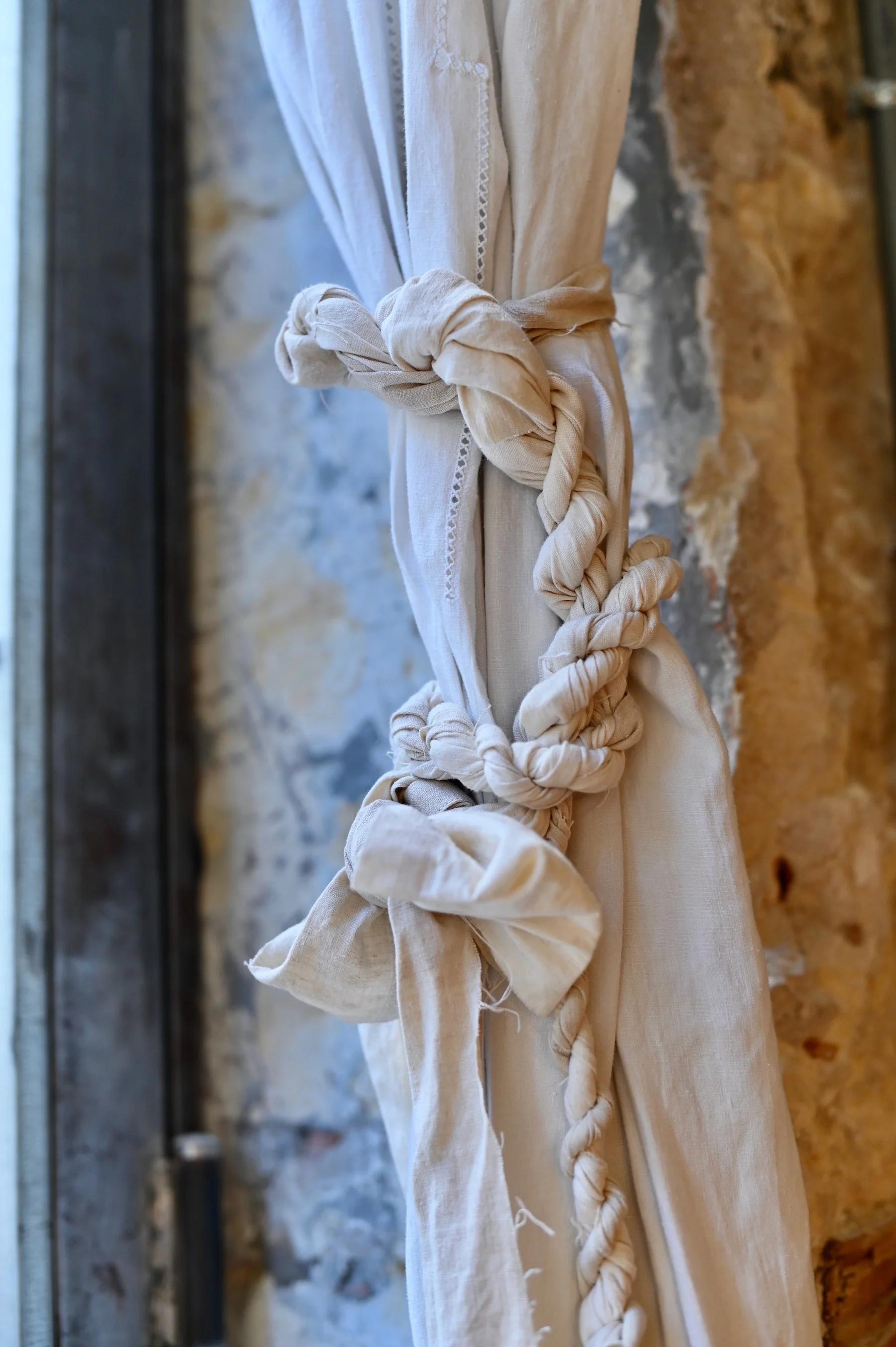 Close-up of beige curtains tied back with creative knot. Textured stone wall background.