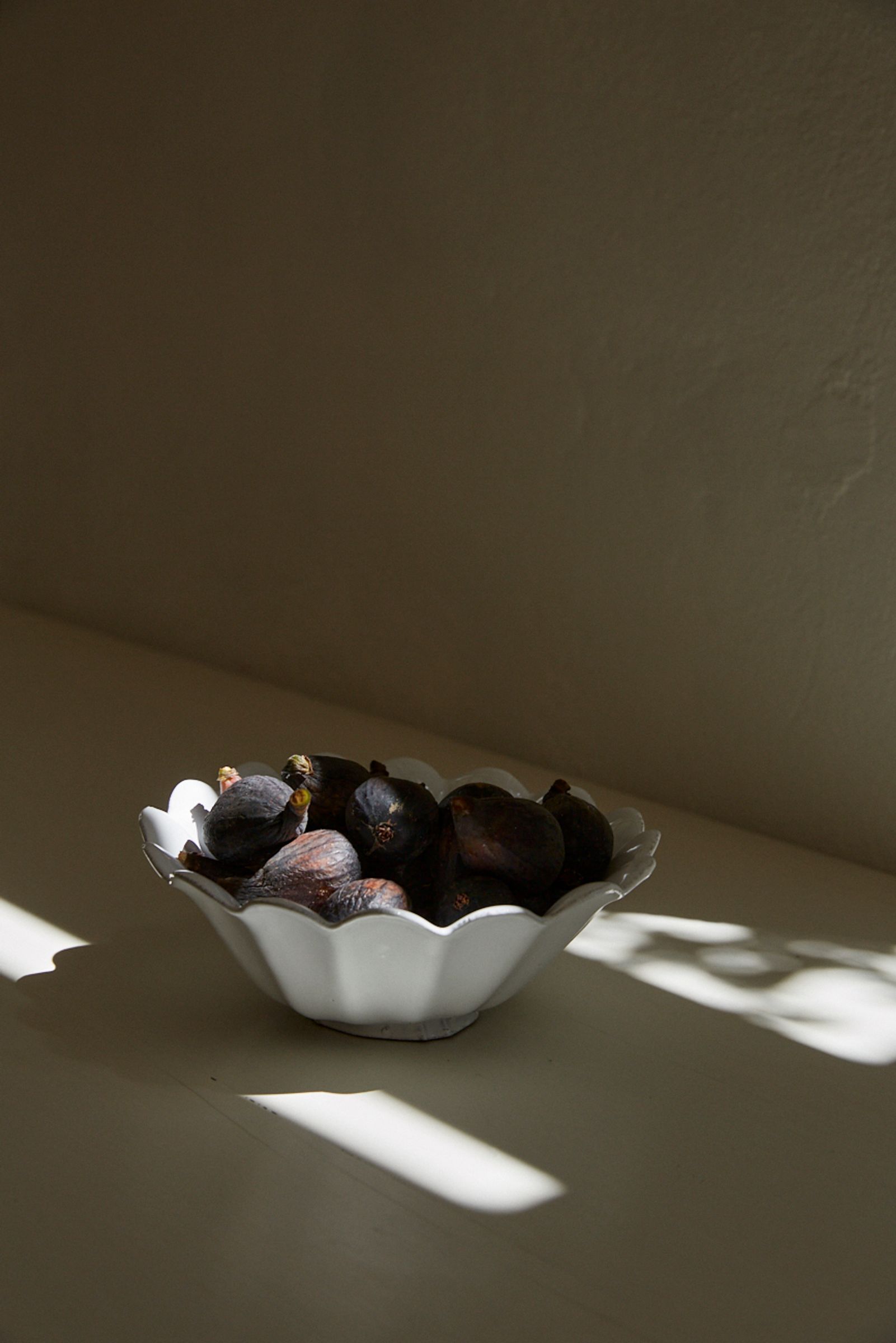 figs sit inside a ceramic bowl in shafts of sunlight