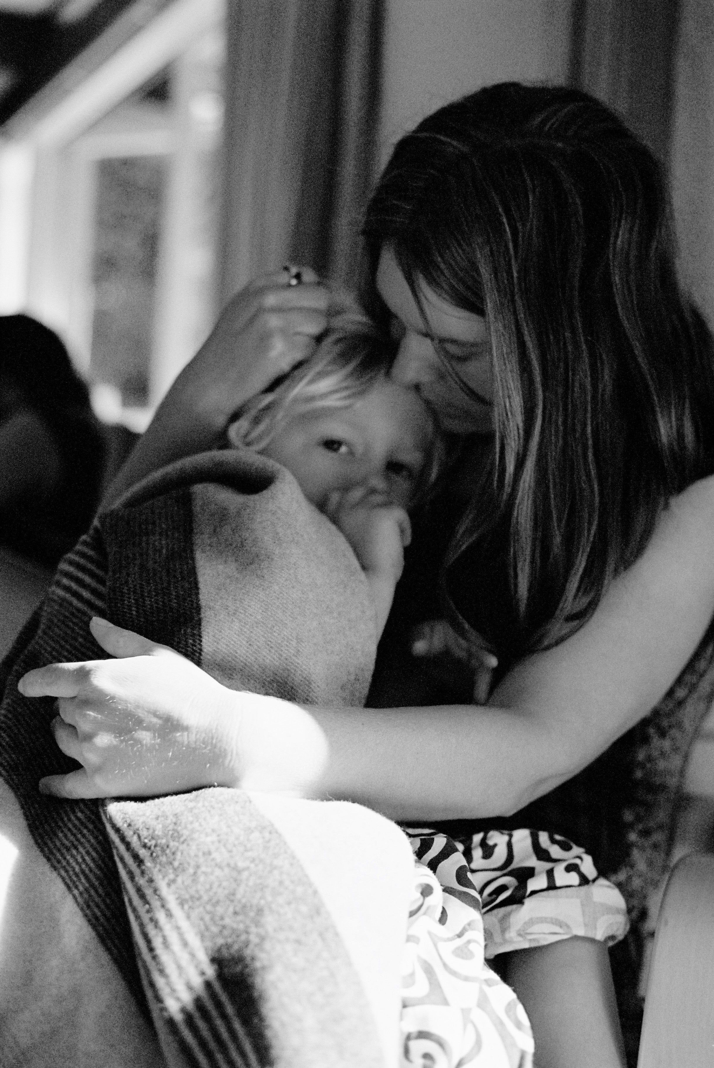 Black-and-white photo of woman embracing blanket-wrapped child. Tender, intimate moment.