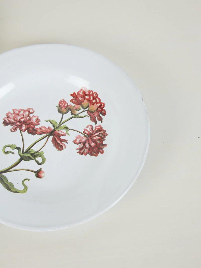 White plate with red and pink flower design on beige surface. Green stems and leaves complement the flowers.