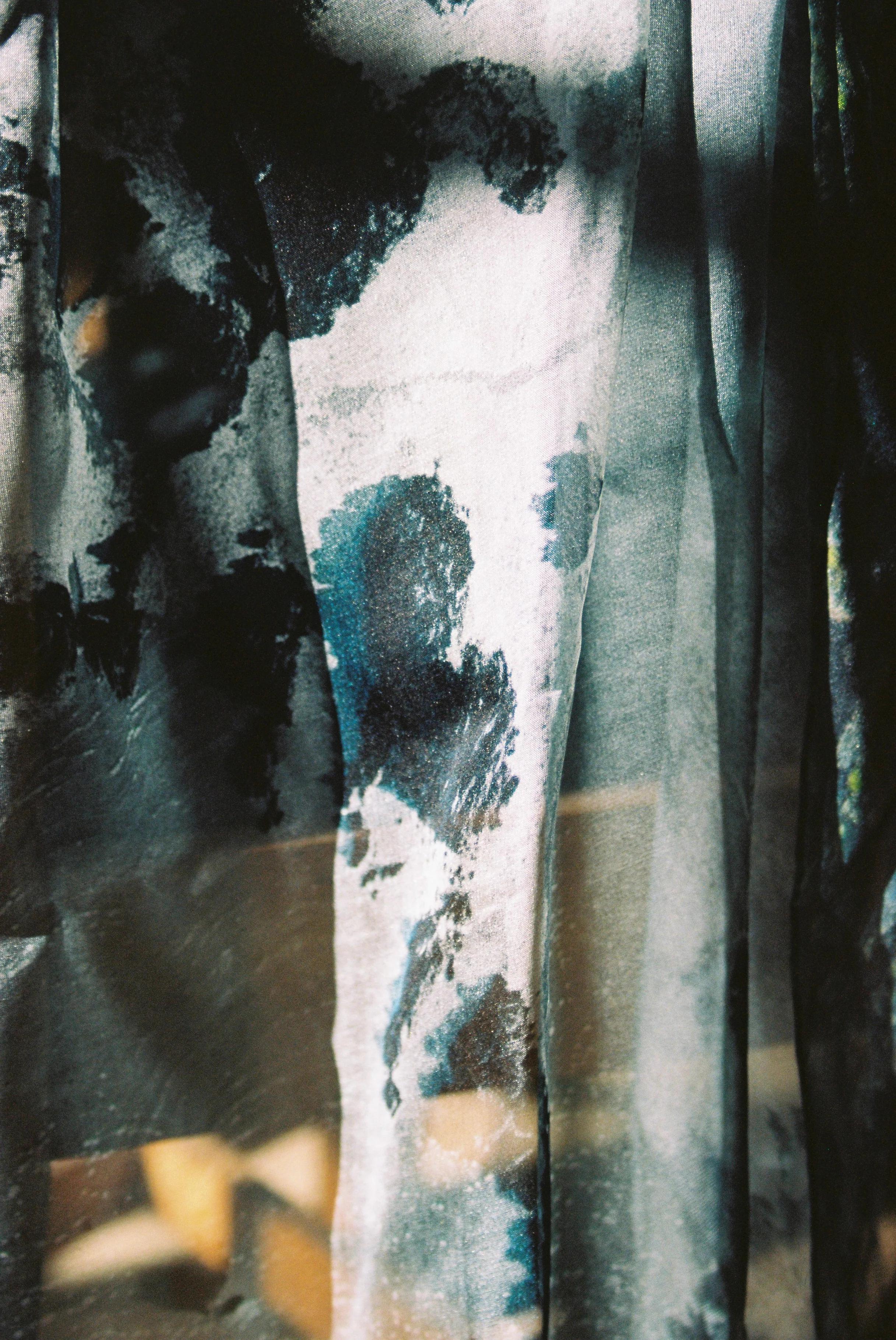 Close-up of sheer fabric with mottled black and grey patterns. Light and shadow play across textured surface.