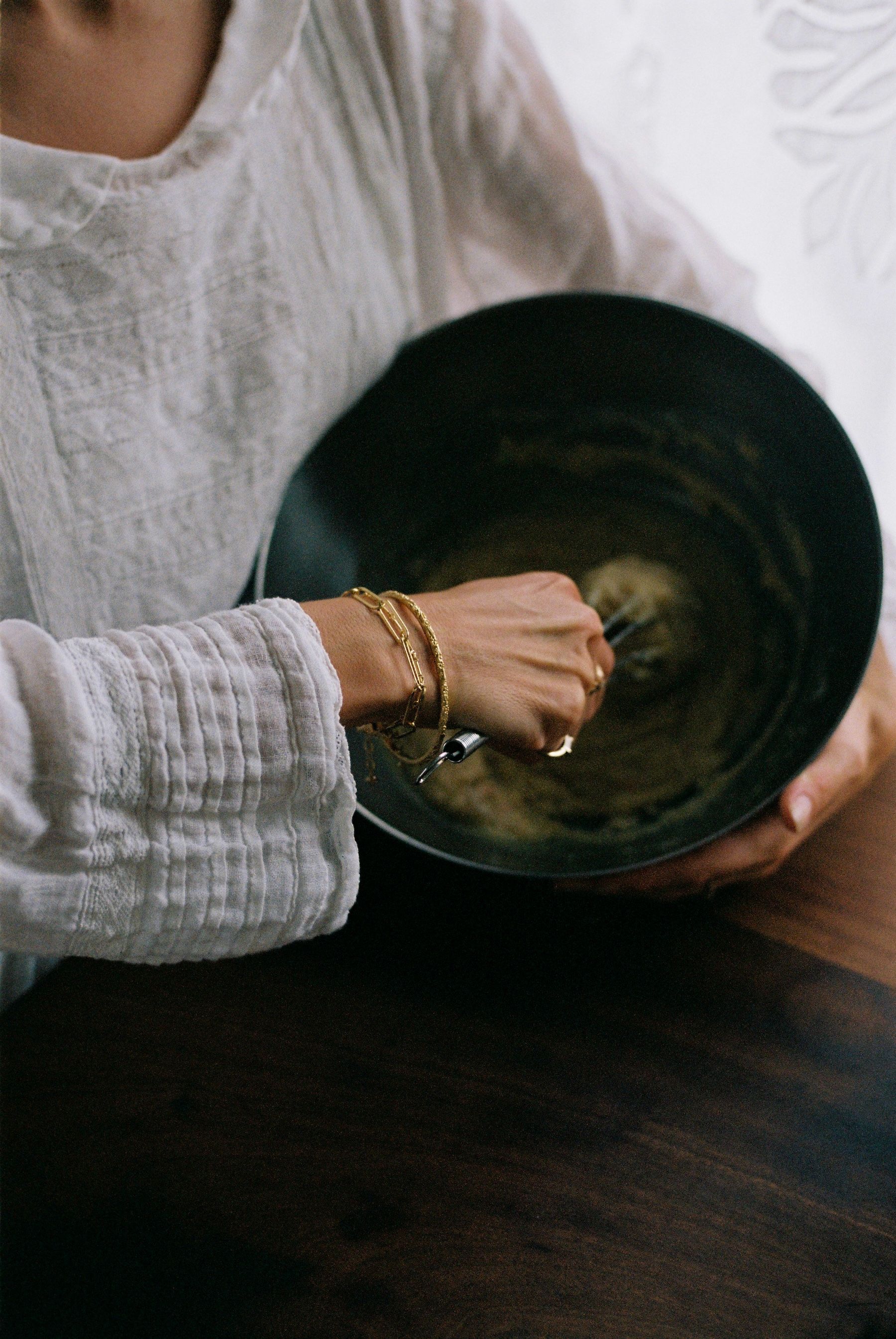 woman wearing a soft white dress and gold bangles mixes cake mix in a large bowl 