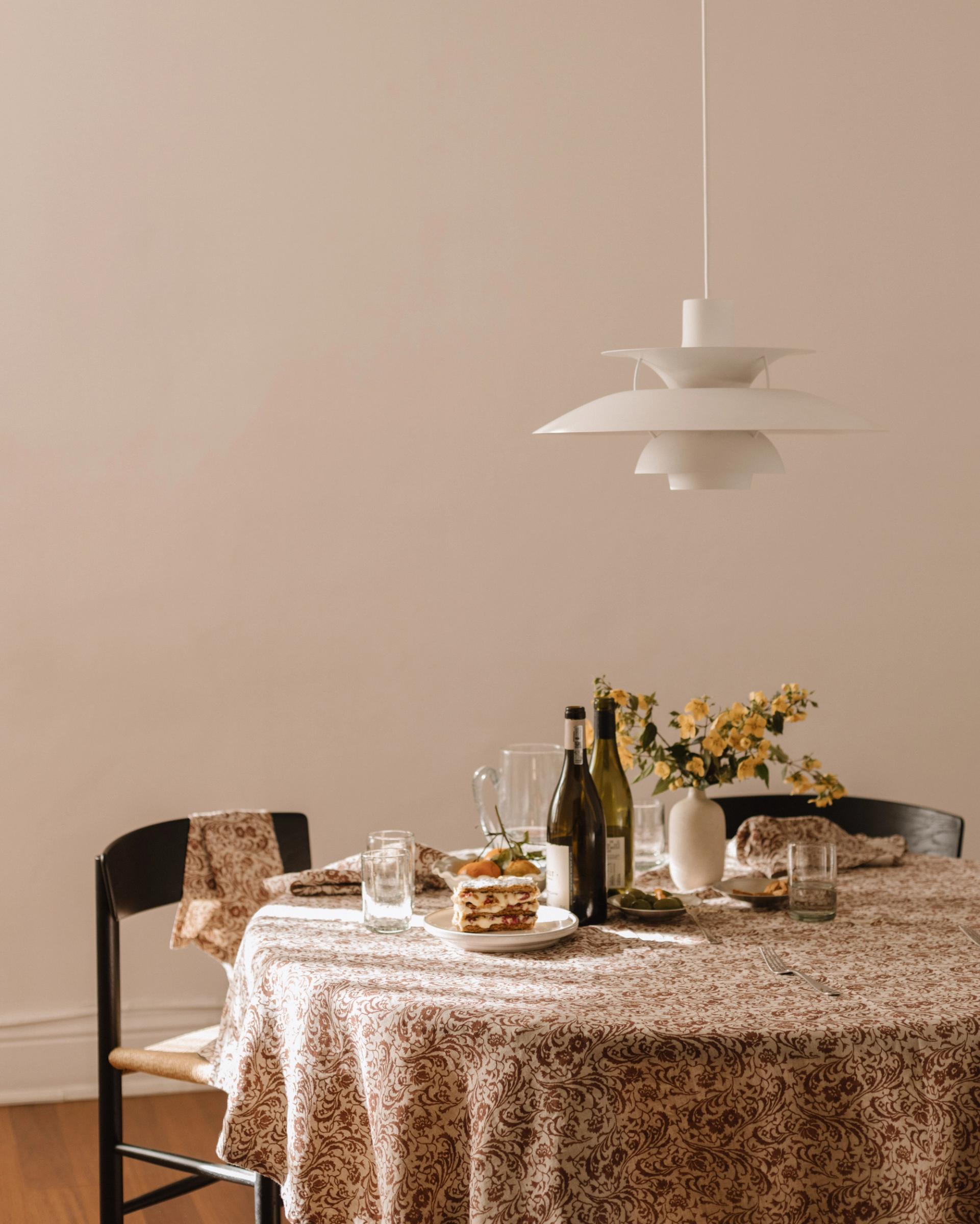 a round table covered in red and cream printed tablecloth with a black chair and white lamp