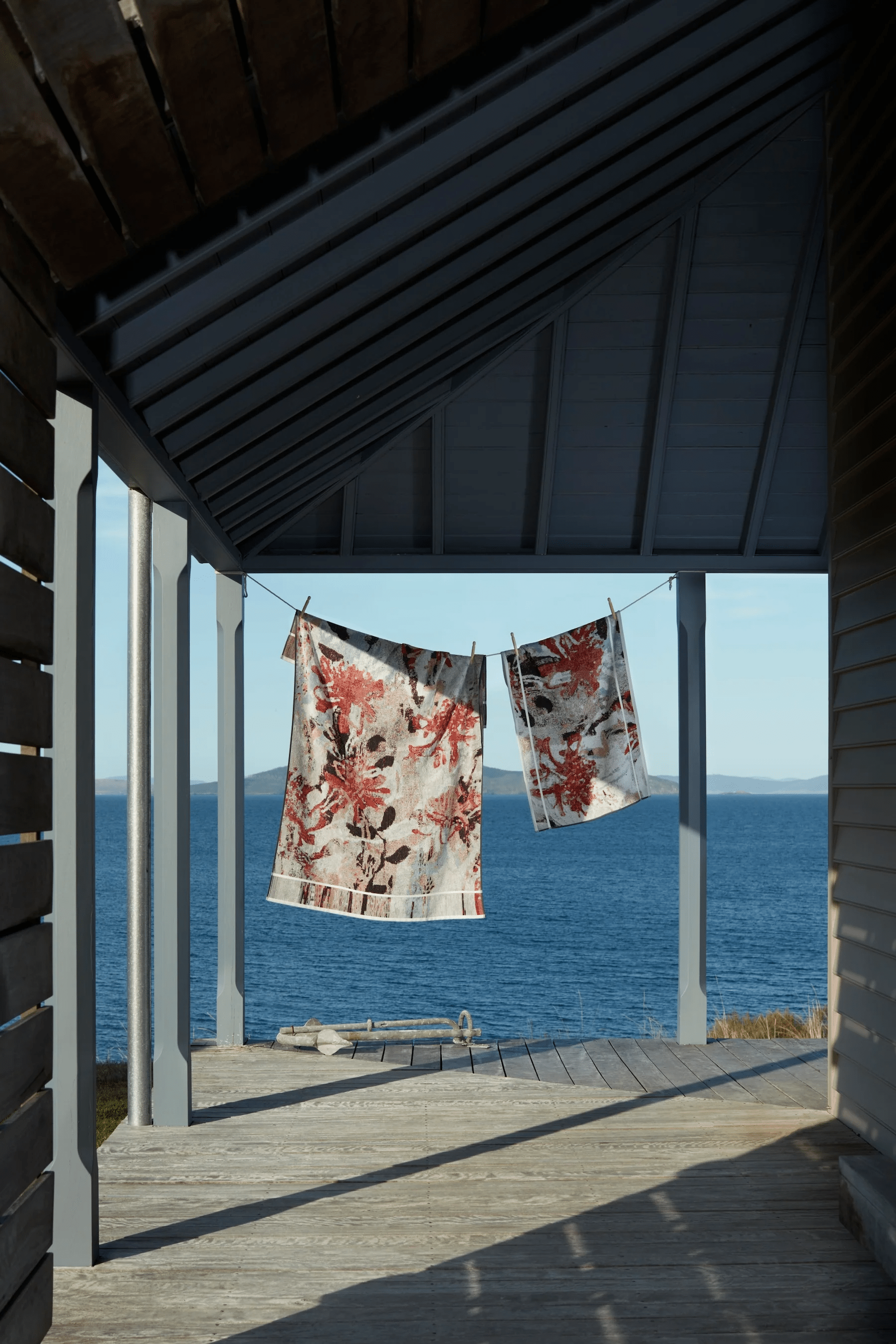 Patterned towels on seaside porch clothesline. Ocean and Australian landscape in background.