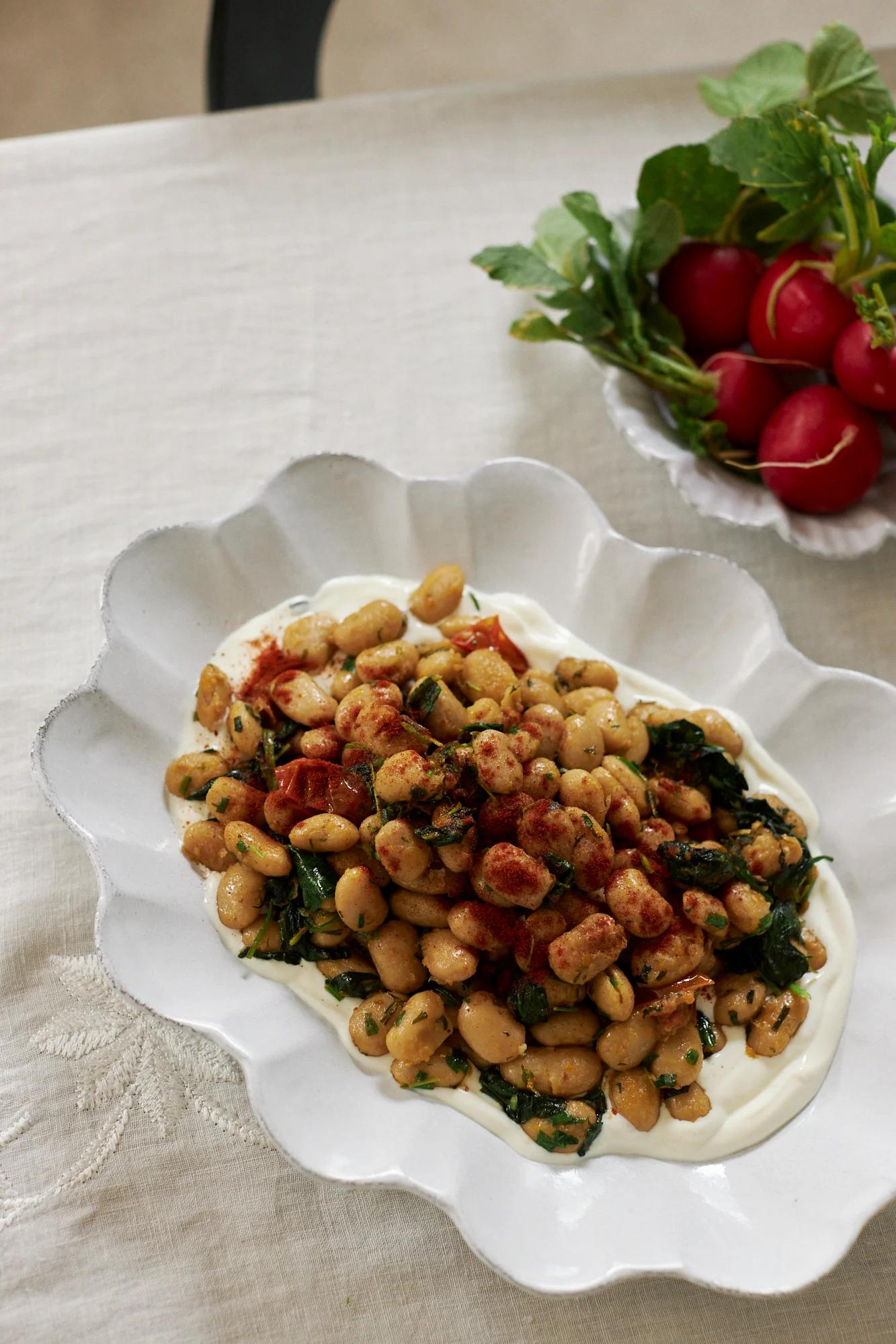 A scalloped dish with bean salad on a cream tablecloth. Radishes in the background add colour, perfect for a restful Easter break.