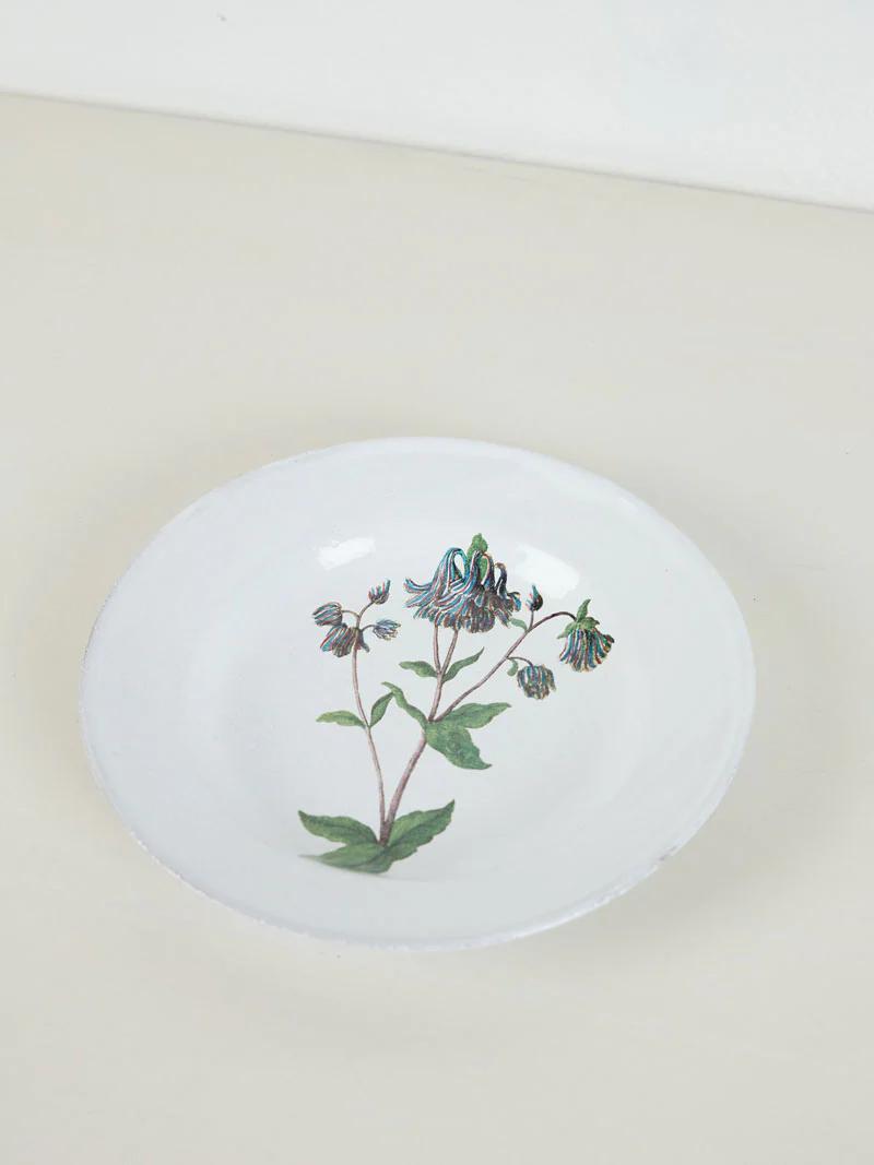 White plate with green and black bell-shaped flower design. Placed on light surface against plain background.