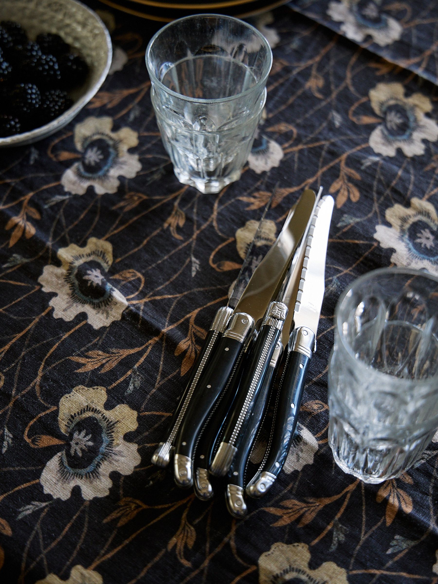black handled knives sit bundles on a dark floral tablecloth