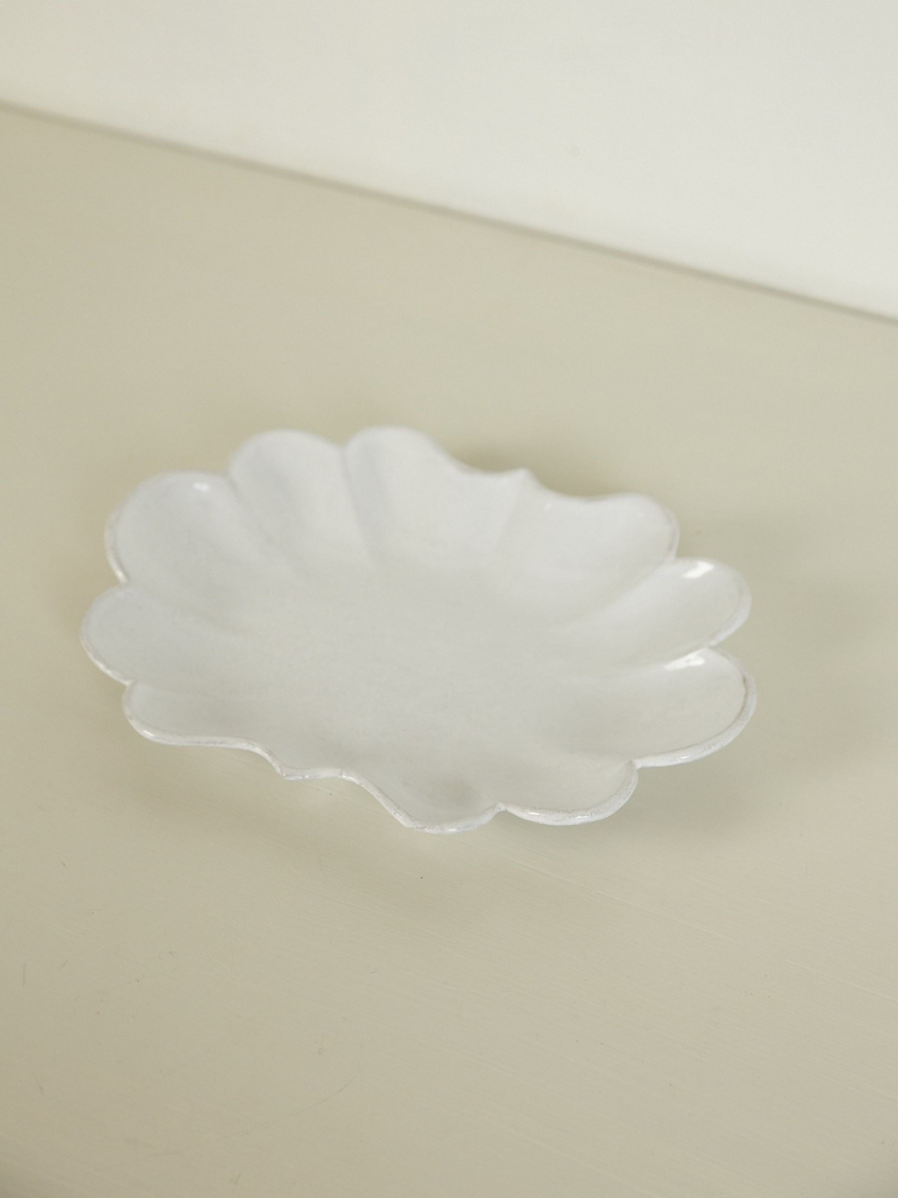 Empty white oval porcelain plate with scalloped edges on light beige surface. White background.