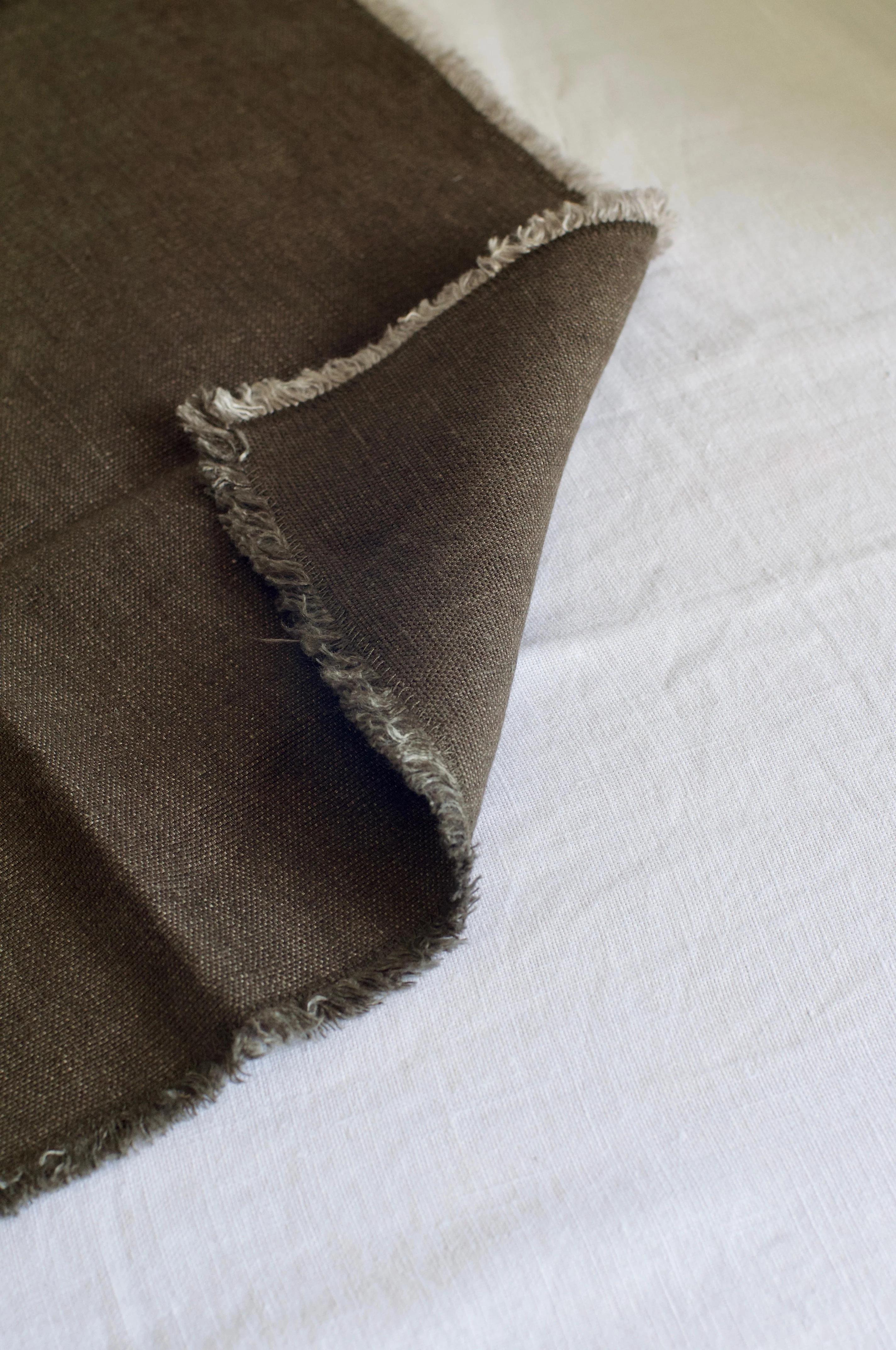 Close-up of dark brown frayed fabric on white. Textured linen partially folded. Contemporary Italian design on white background.