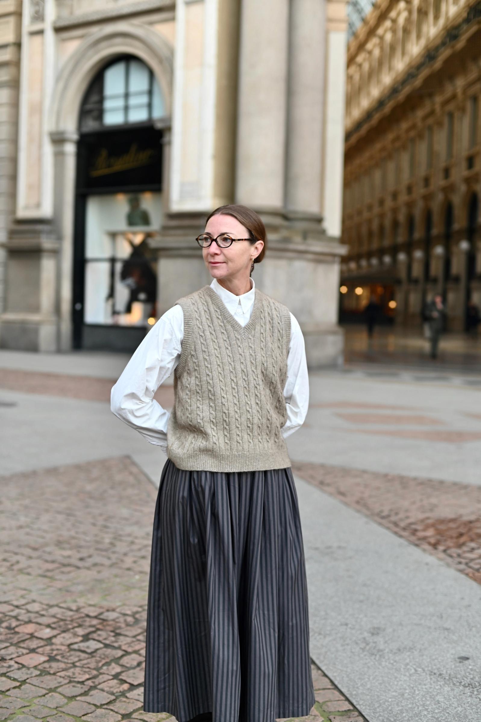 woman dressed in wooden vest skirt and shirt stands at entrance to halls in Milan