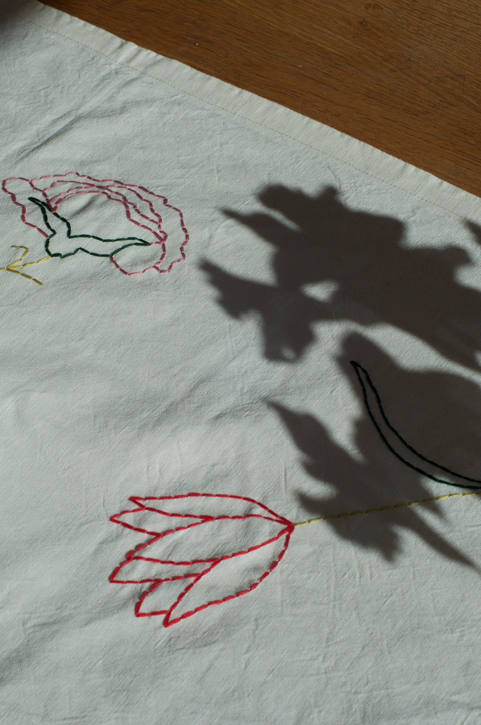 Fabric with colorful flower embroidery. Red tulip, pink and green stitching. Dark shadows cast on fabric.