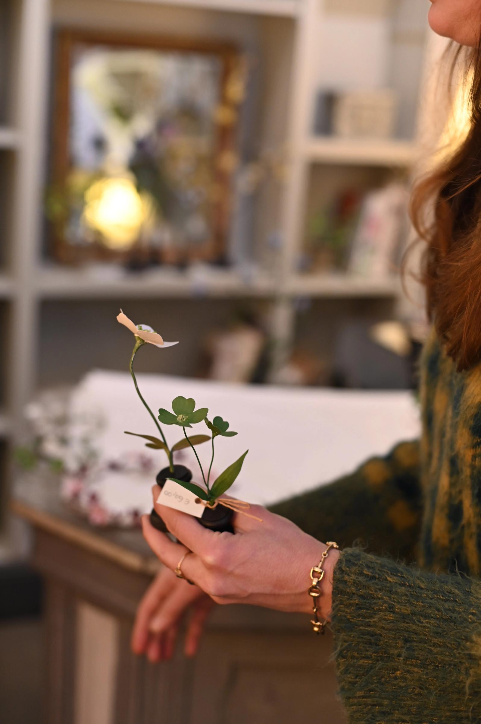hand holding a small flower sculpture with green leaves