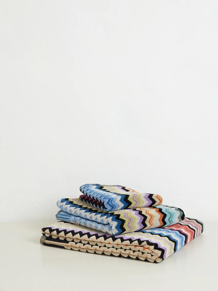 Three folded towels with a colourful zigzag pattern in blue, green, yellow, pink, and black, stacked on a white surface.