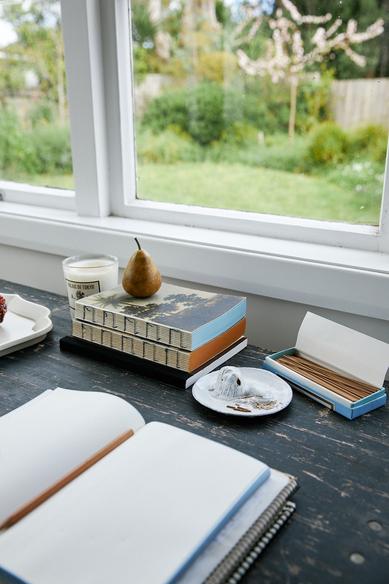 Notebook open on desk with a pile of notebooks set against a windowsill