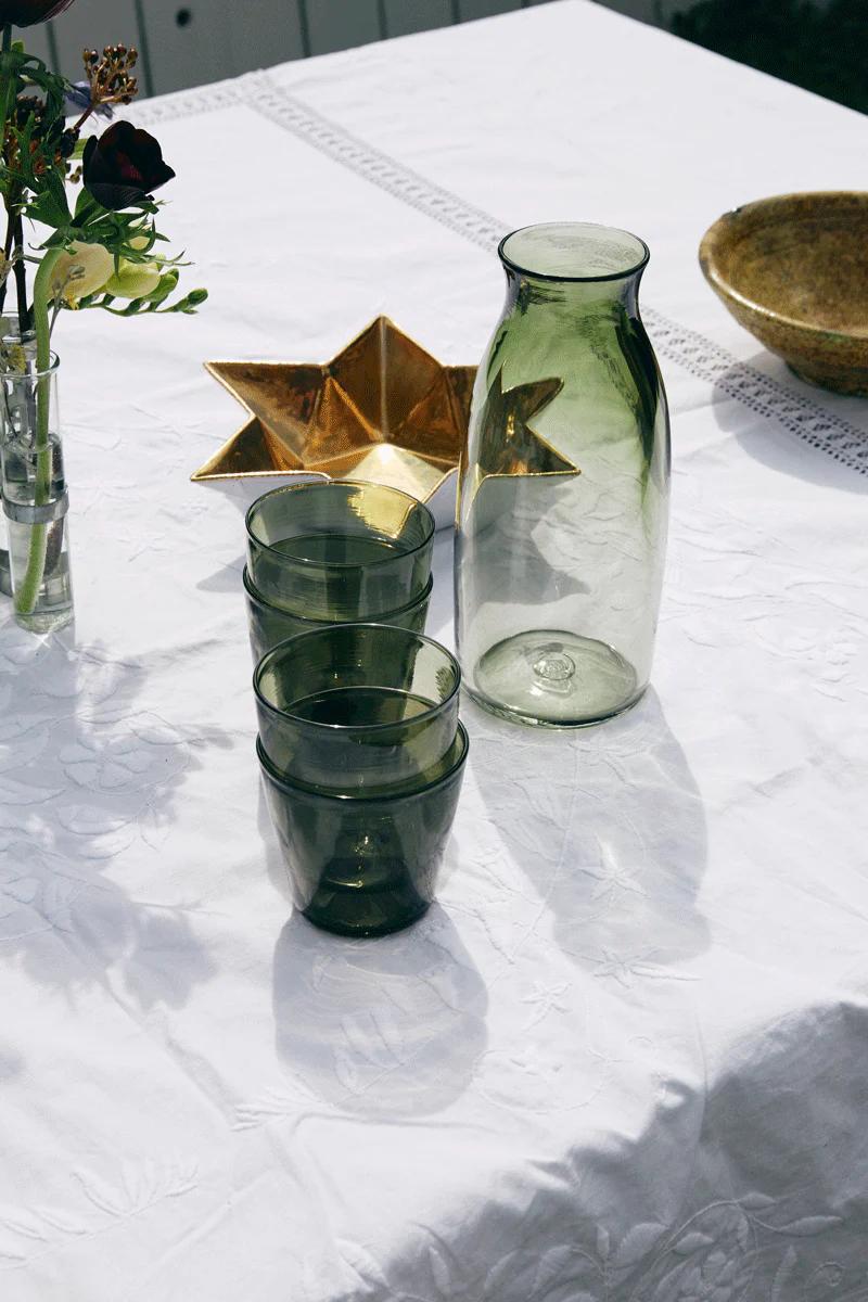 Table with green glassware, gold star dish, and brown bowl. Small flower vase on white tablecloth.