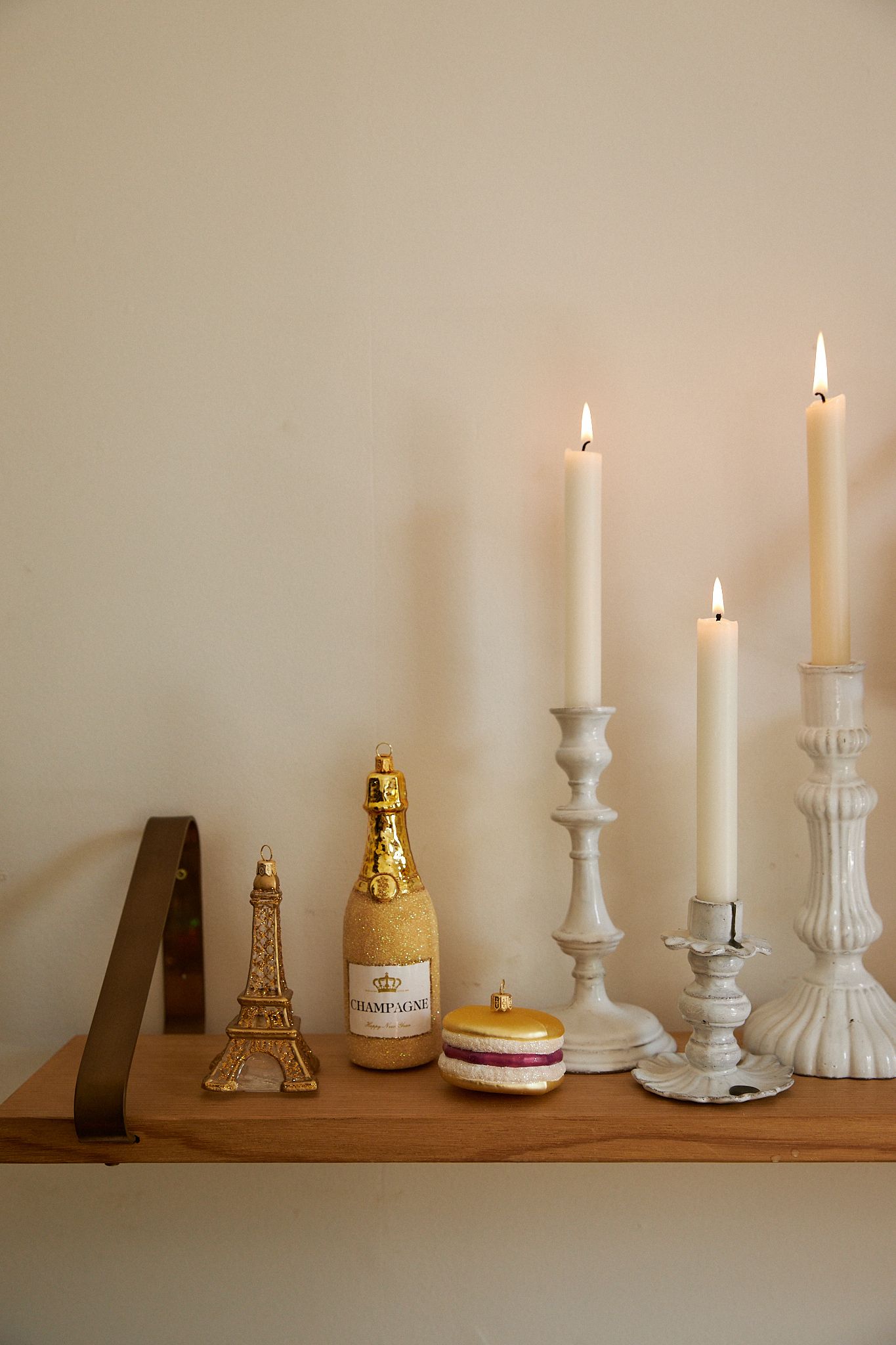 A wooden shelf hosts three different sized candle holders and decorations