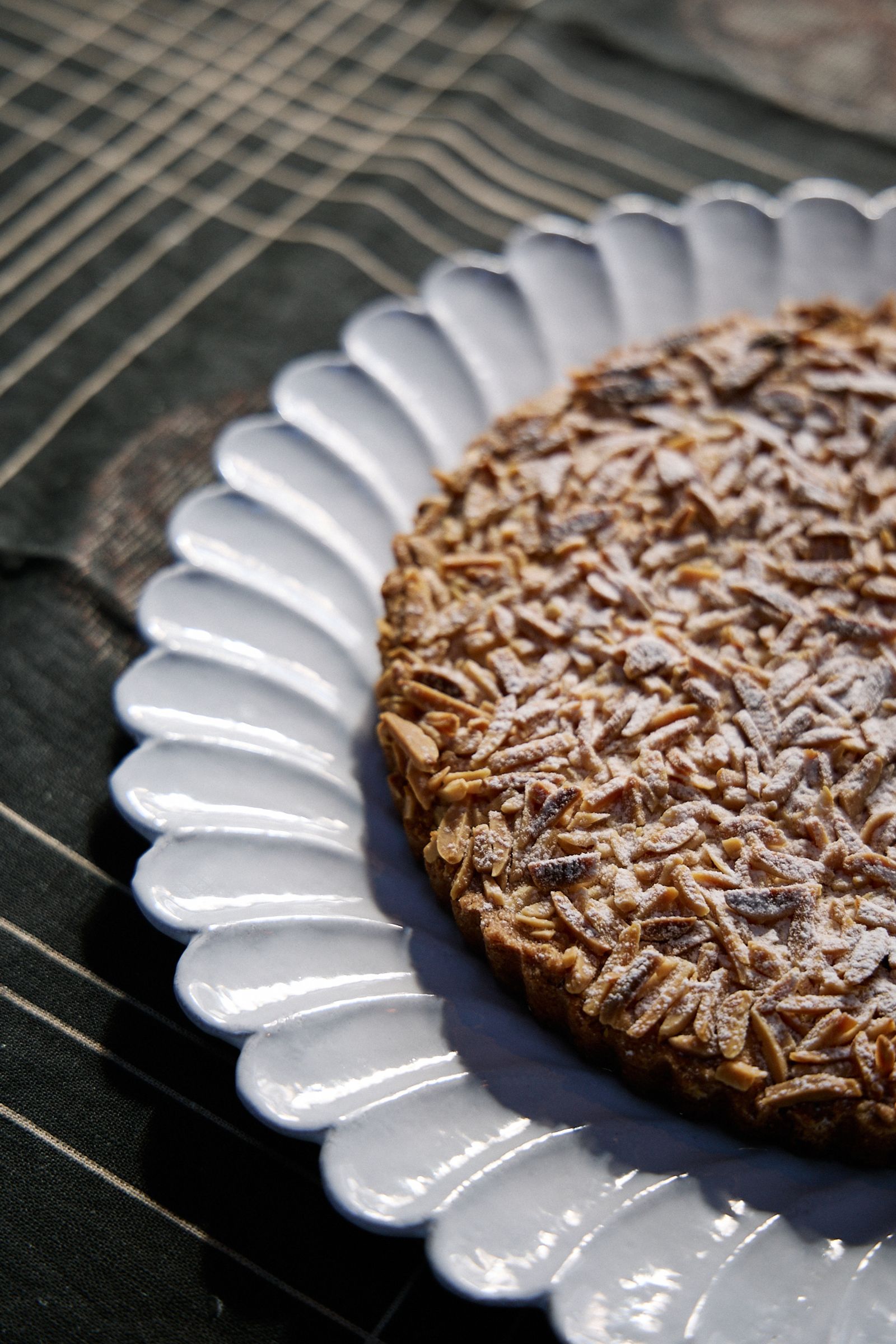 cake sits on a scalloped plate in the sun on a dark tablecloth