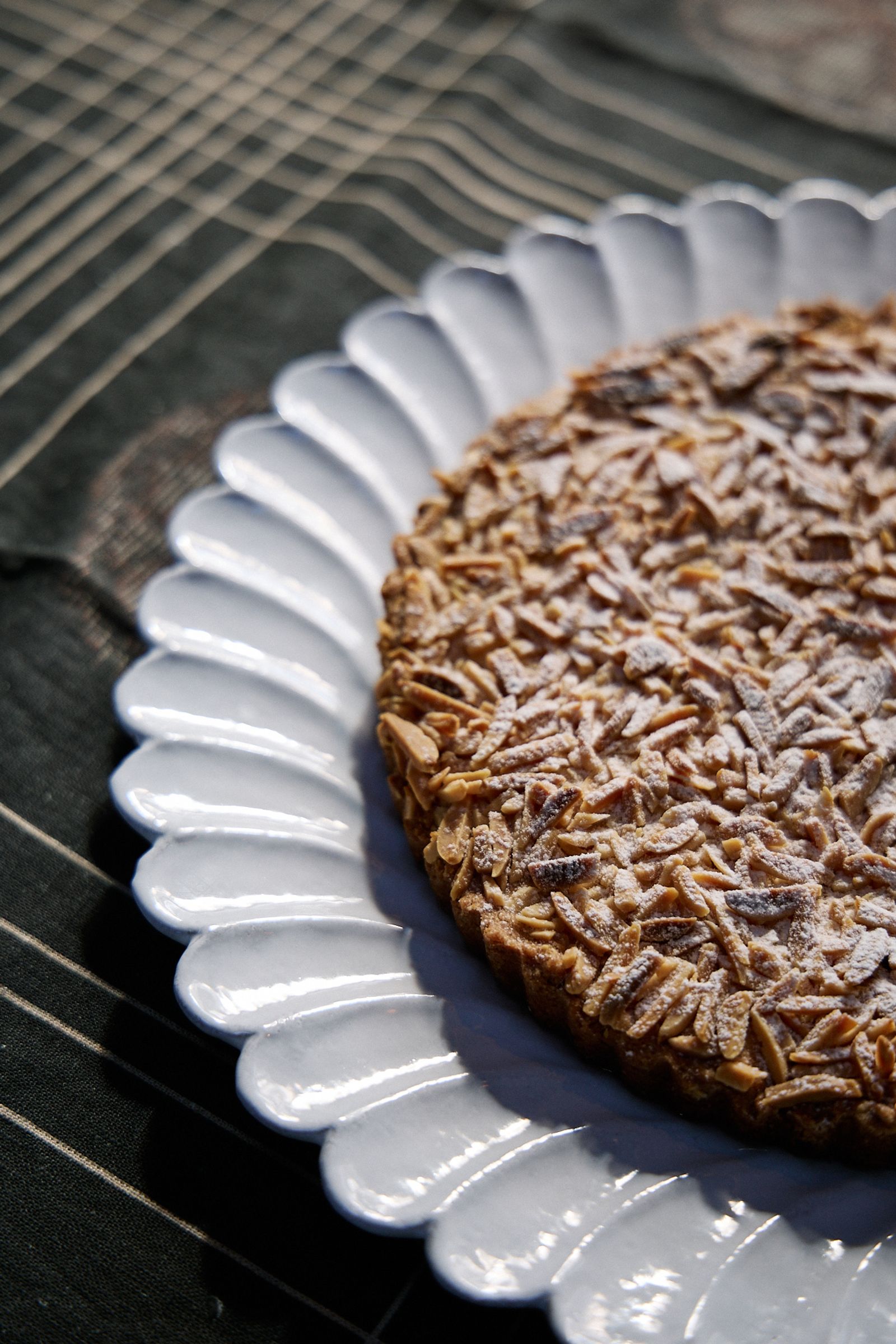 cake sits on a scalloped plate in the sun on a dark tablecloth