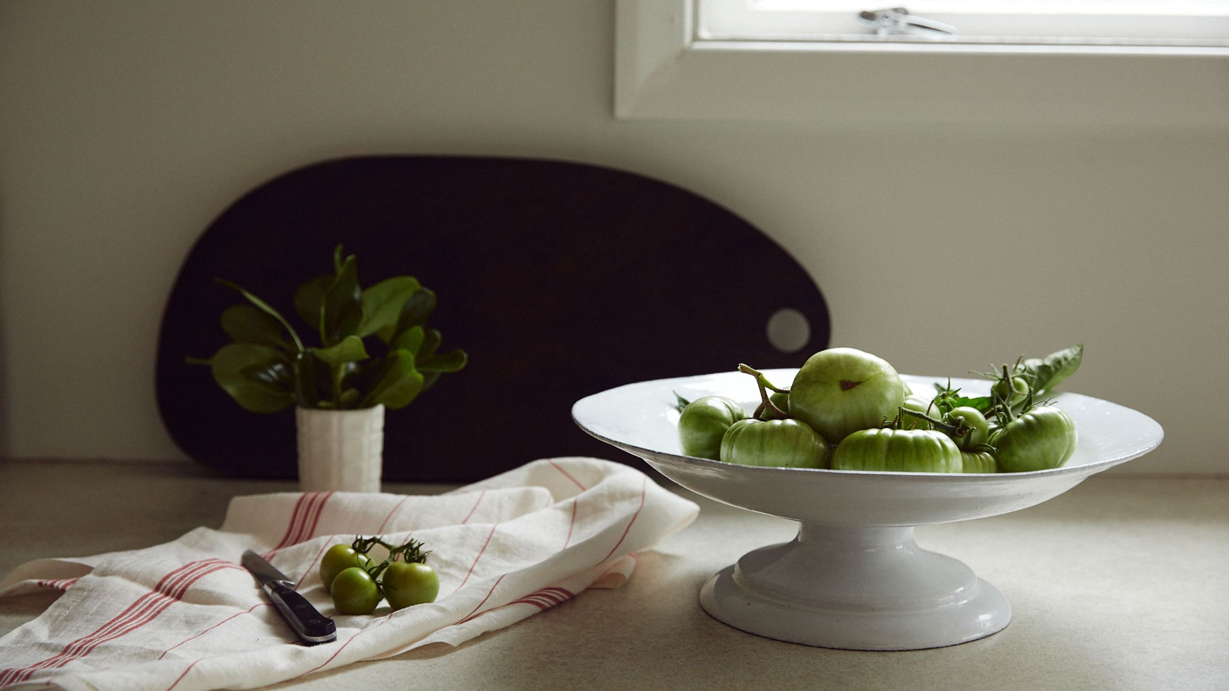 Ceramic fruit stand with green tomatoes on kitchen bench