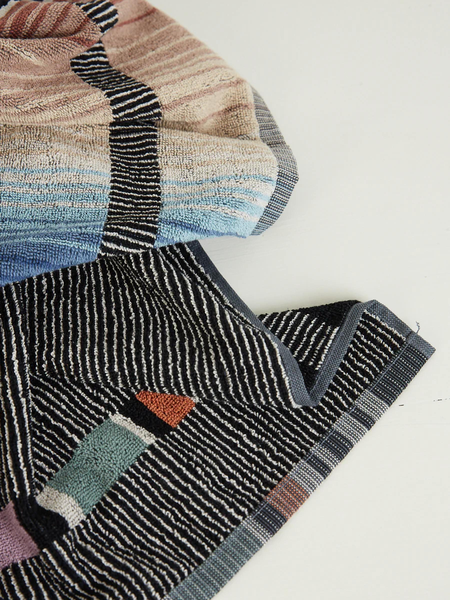 Close-up of two draped towels: one in pastel shades of blue, pink, and beige; the other with a dark background and geometric accents.