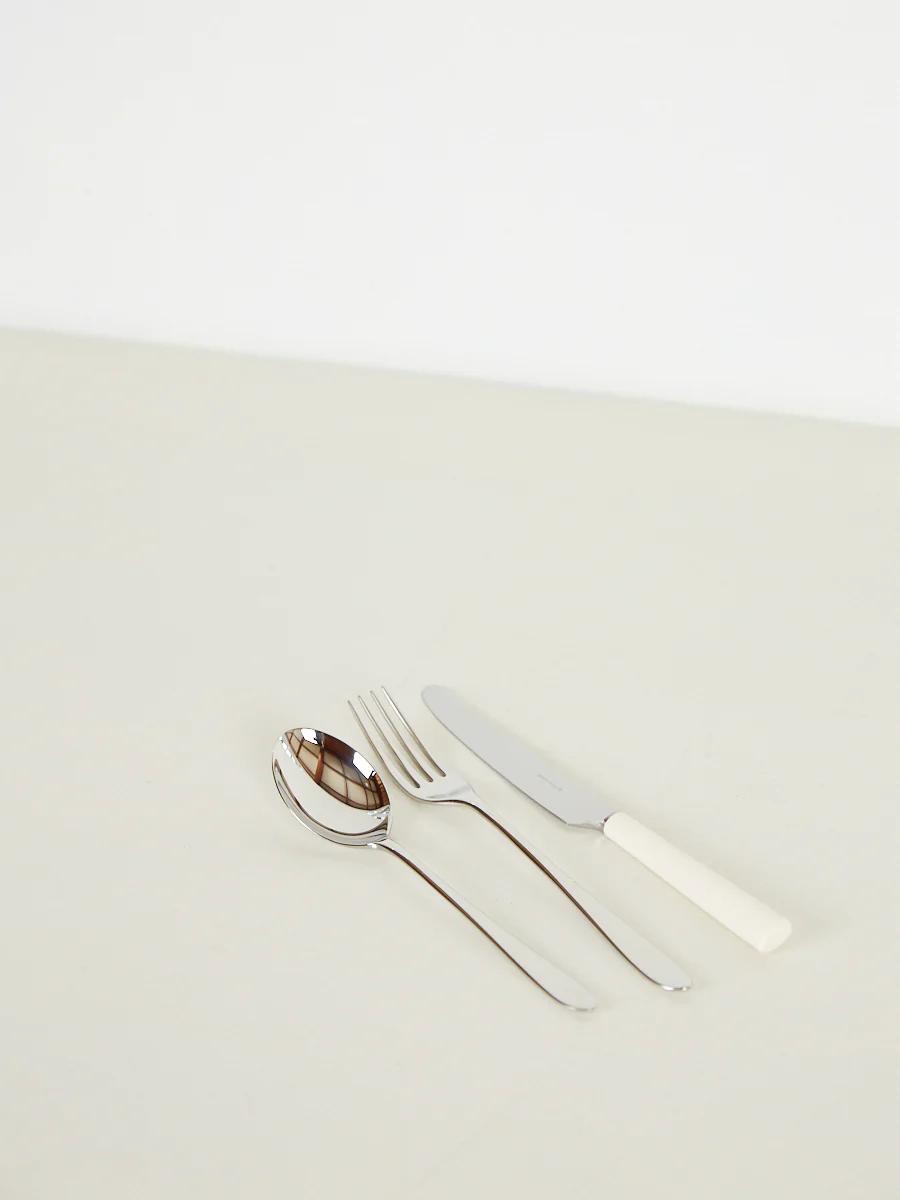 Spoon, fork with steel handles, white-handled knife on white surface. Plain background.