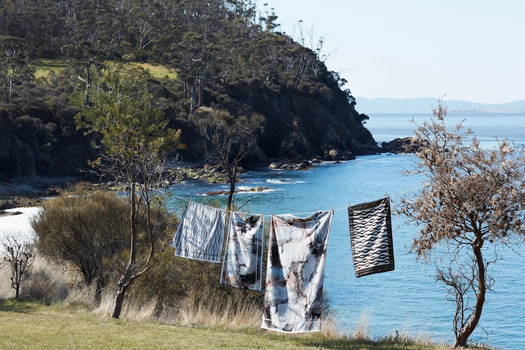 Colourful towels on clothesline between trees. Rocky cliffs, ocean, and hills in background.