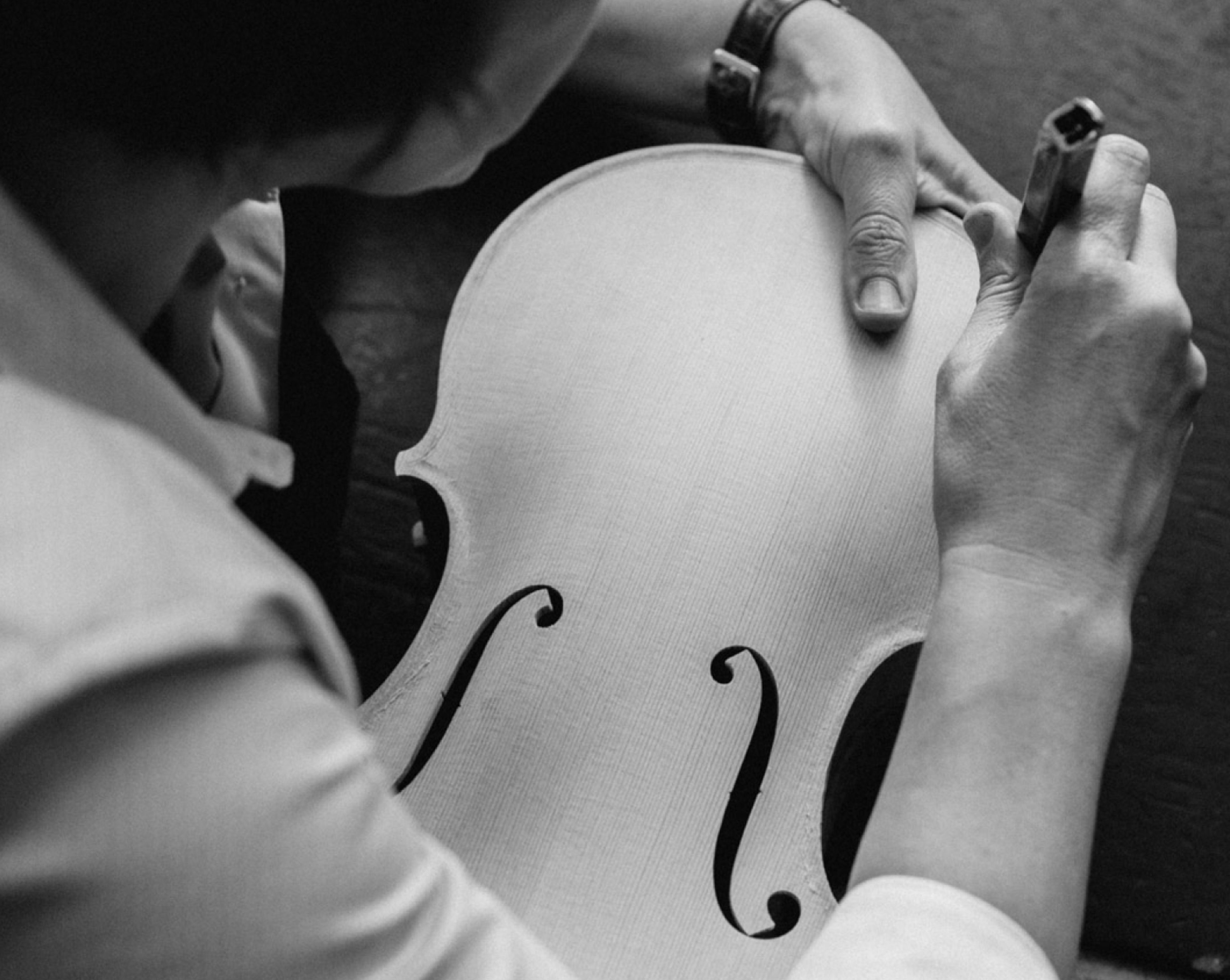 Hands working on the unvarnished top of a violin.
